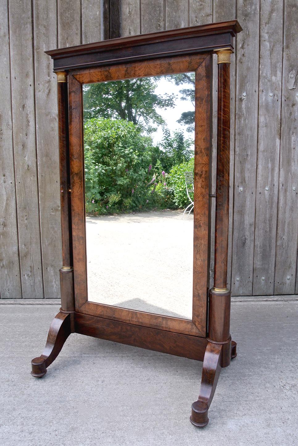 An impressively large and beautiful English cheval mirror of particularly fine quality and dating from c.1815.

Of French Empire design, the original frame with substantial tapering columns of figured mahogany mounted with exquisitely incised bronze