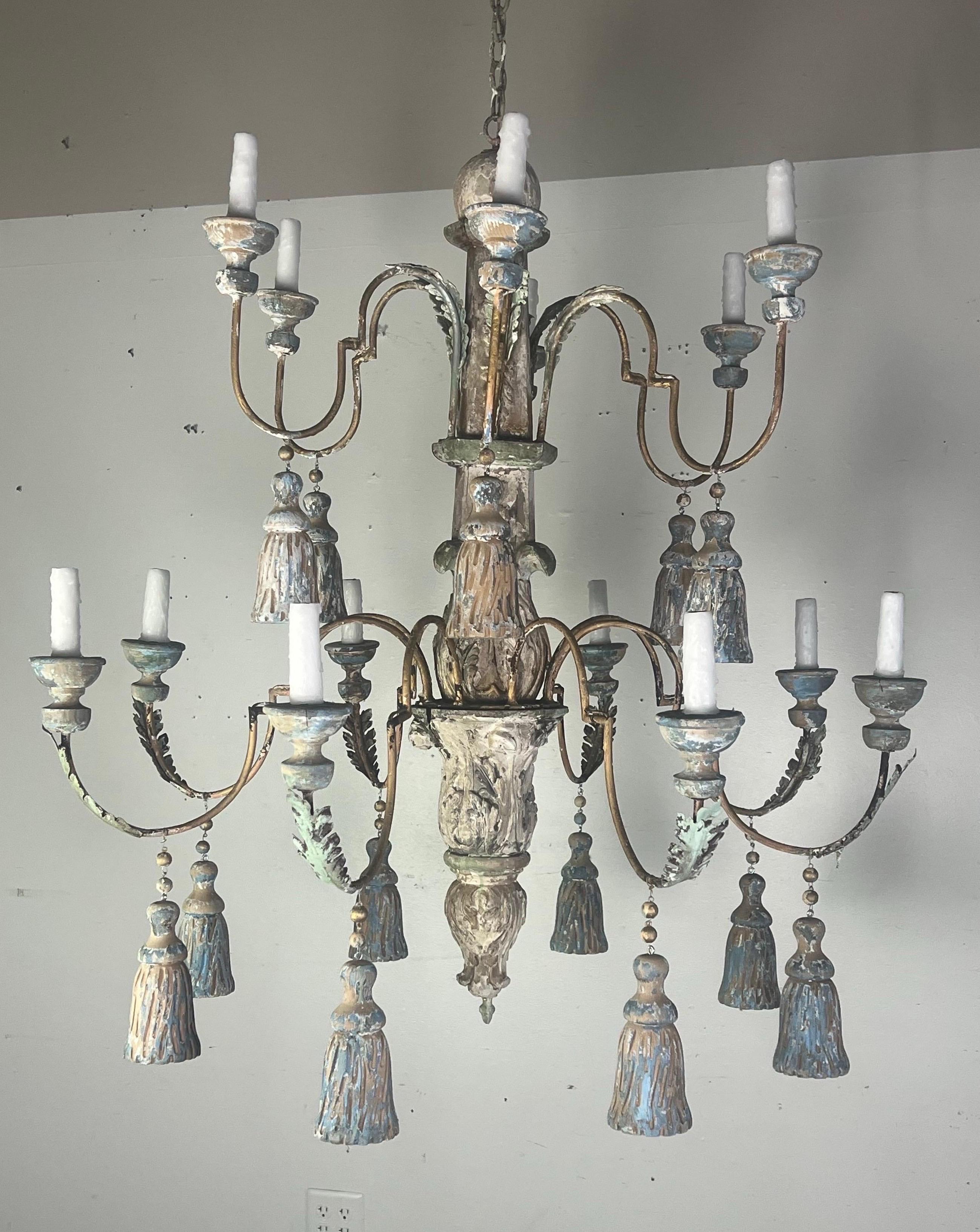 Monumentale lampadario italiano dipinto a 14 luci con nappe in legno intagliato.  Il lampadario ha una colonna centrale prominente che funge da struttura principale, da cui si estendono i bracci.  I bracci sono elegantemente ricurvi e ciascuno di