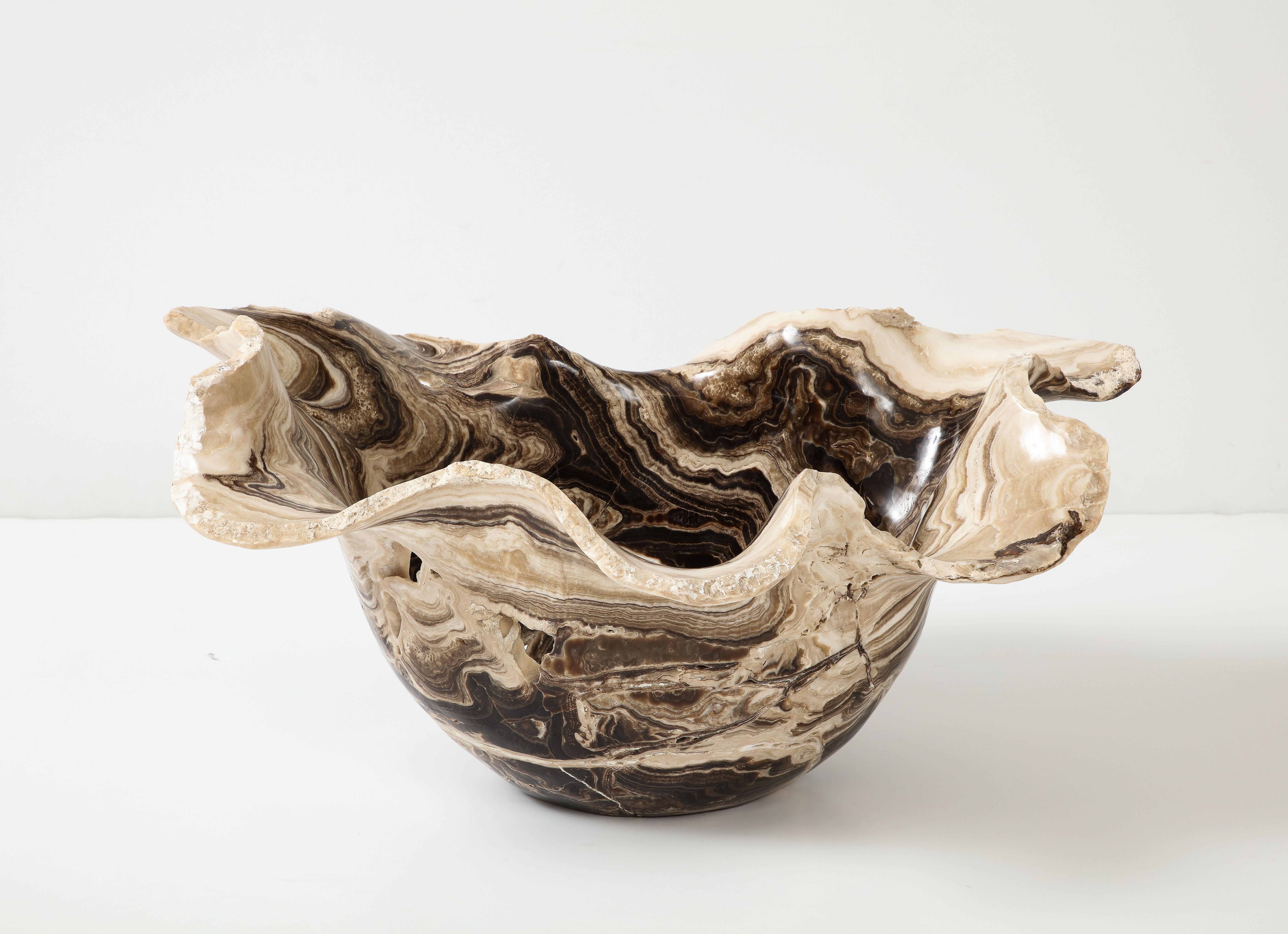 A monumental sculptural hand-carved onyx bowl with an undulating scalloped live edge in shades of deep chocolate brown, cream, white and beige. The coloration and proportion of this bowl are rare and striking and the swirls of color punctuated with
