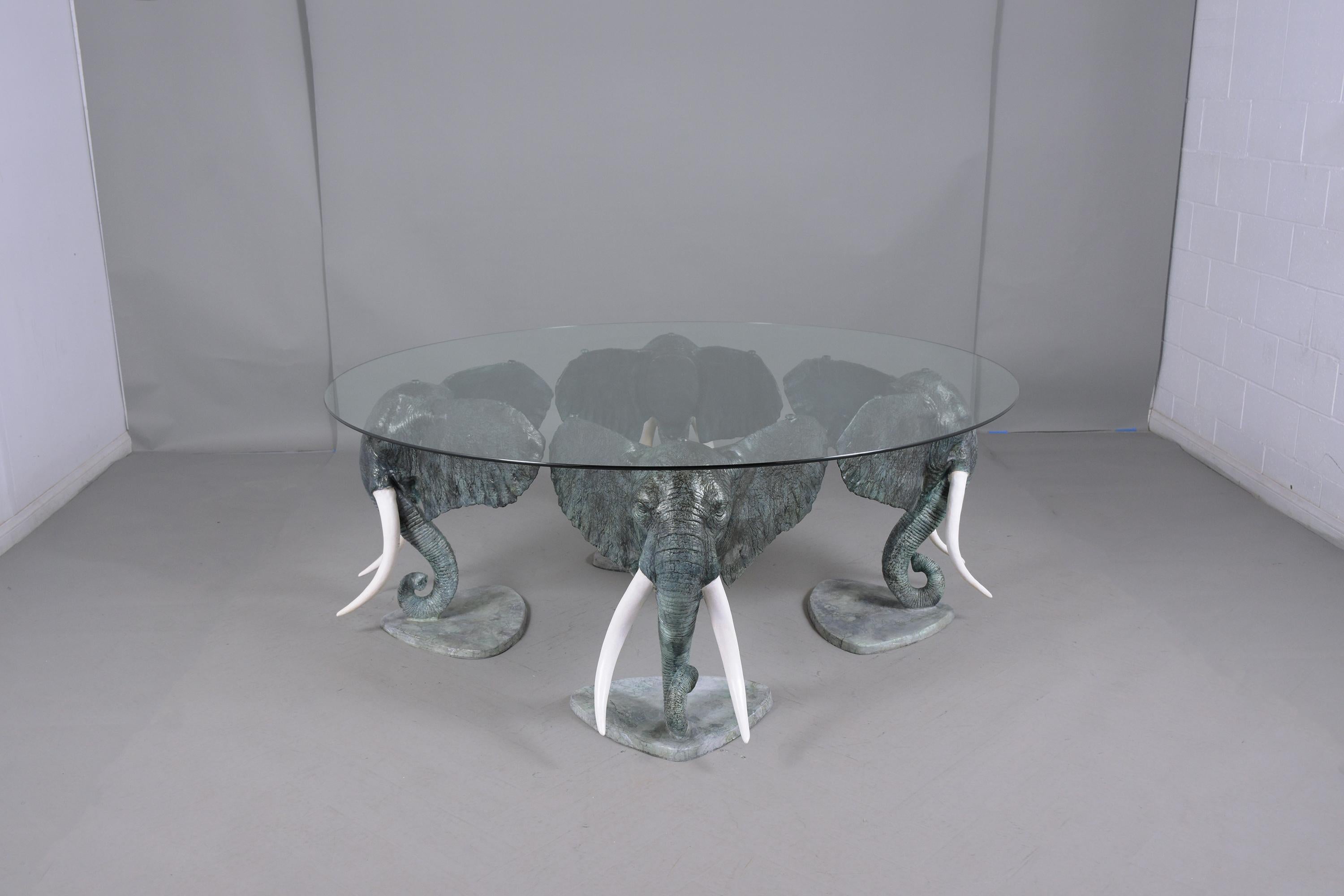 An exceptional sculpture center table features a base made out of four elephant heads crafted out of metal l this intricated and is in good condition. The round center table features a new 3/8 clear glass with flat polished supporting by four