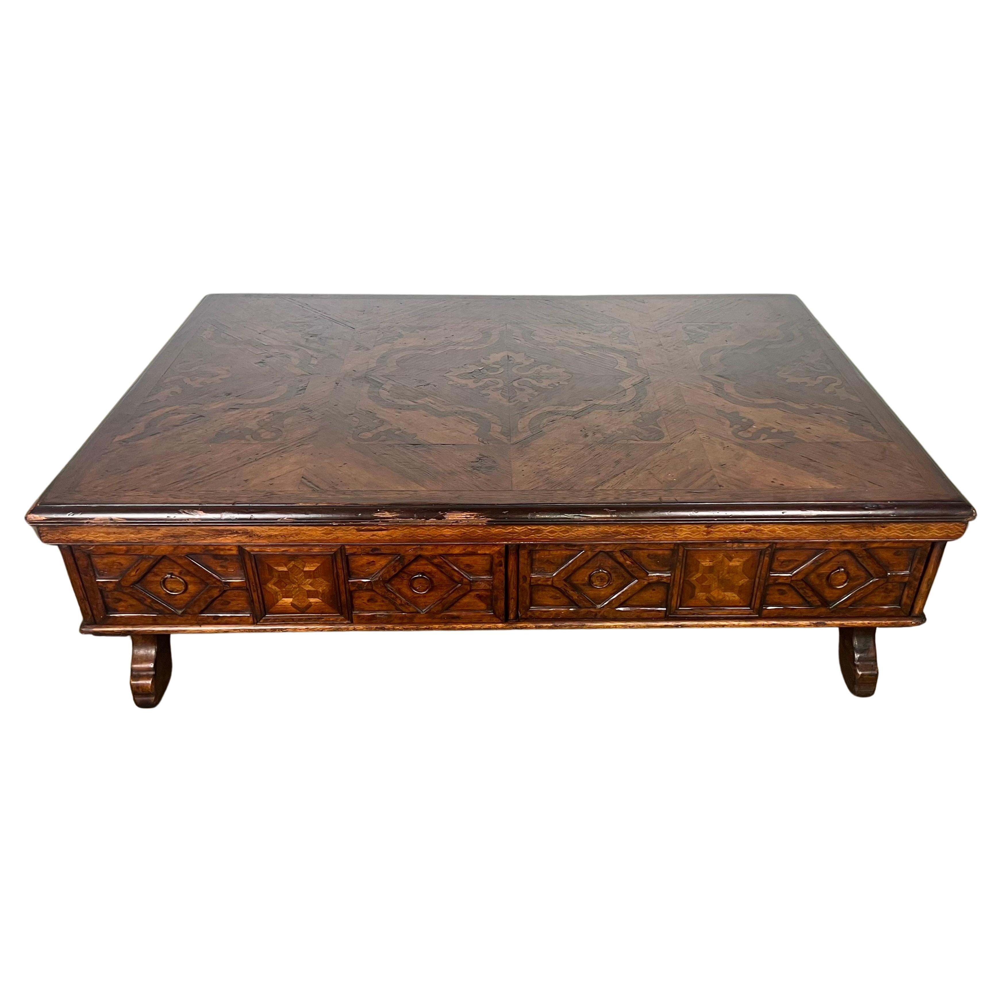 A monumental-sized Spanish coffee table with beautiful carving and an inlaid top featuring pine, walnut, and mahogany.  It is a stunning and functional piece of furniture.  With four drawers and four carved legs, it combines both beauty and
