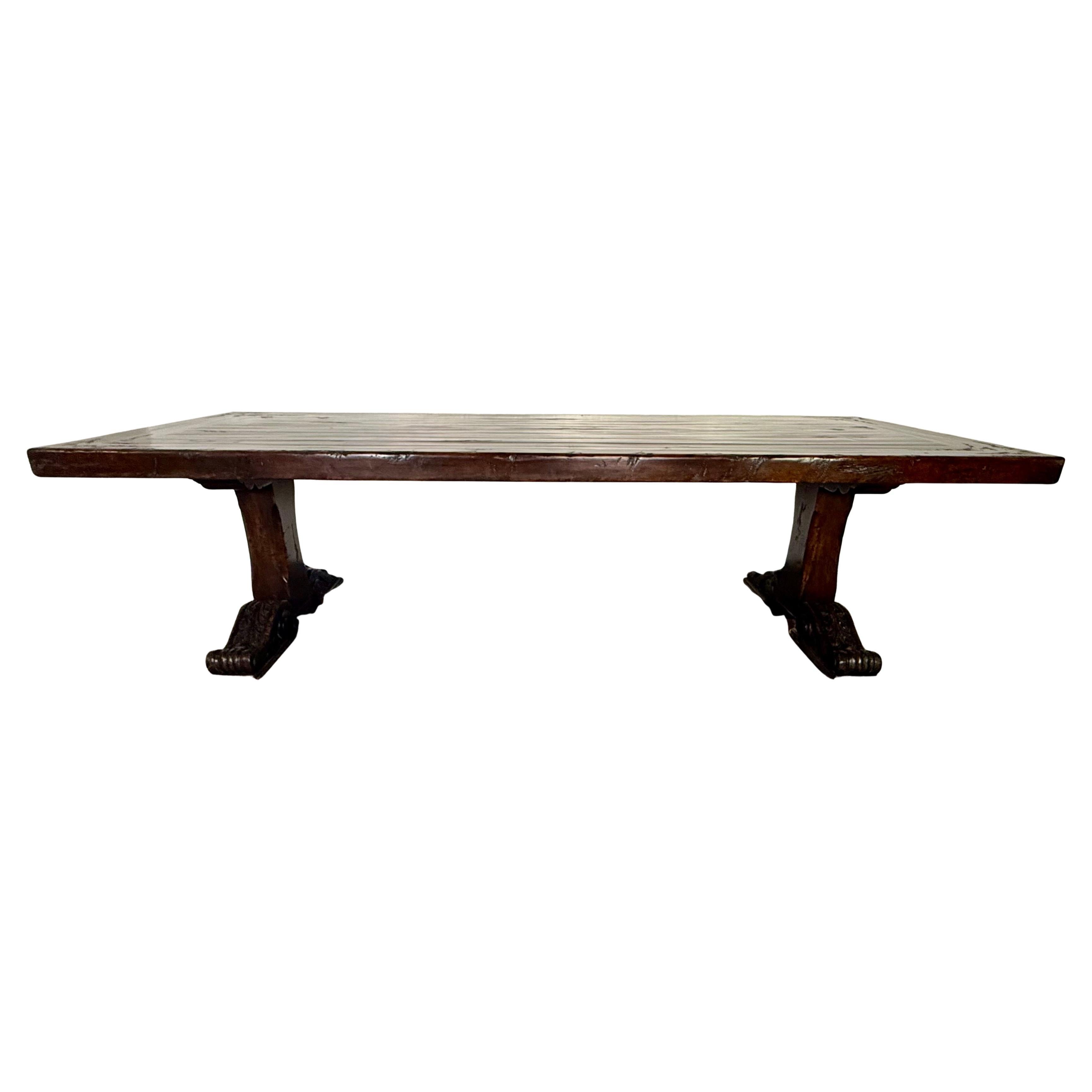 A striking and substantial Spanish Revival dining table, crafted in the early 20th century from richly patinated walnut. The rectangular plank top is thick and weighty, displaying a beautifully aged surface with deep character marks and a lustrous