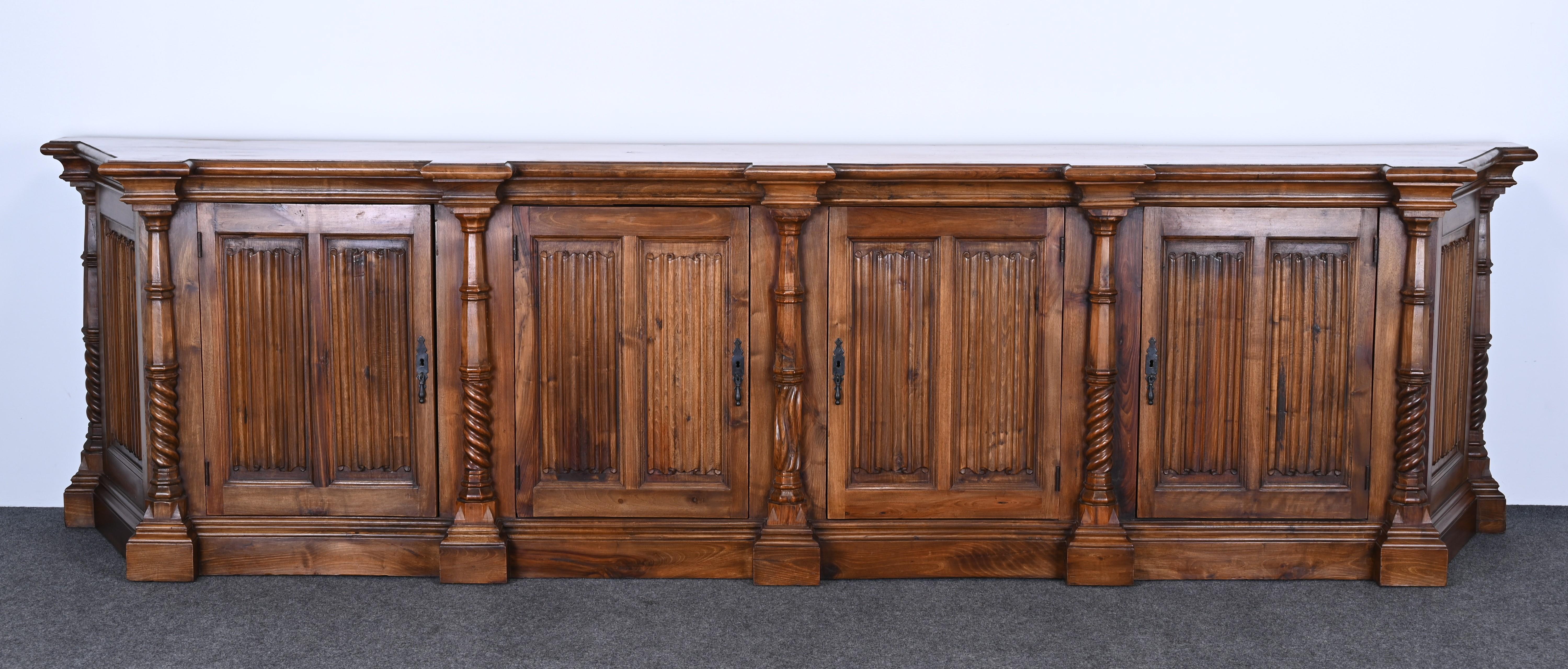 A handsome monumental Spanish Colonial Revival sideboard or credenza. This beautiful piece is hand-carved and was custom-made in Spain and sold in New York in the 1960s. The credenza has 4 doors and 2 drawers for ample storage with 6 adjustable