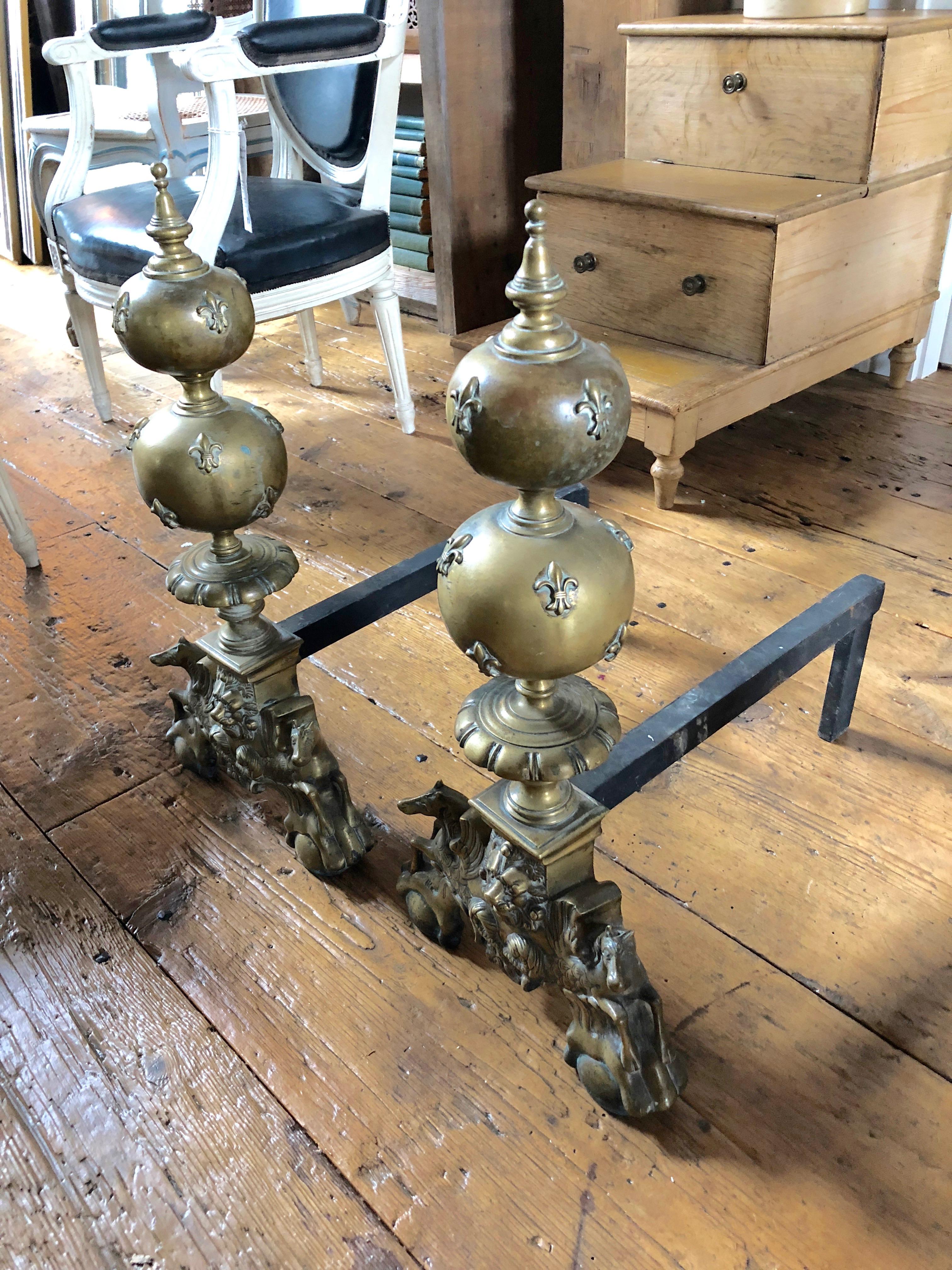 Monumental large pair of andirons, each is surmounted by detailed sculptures of a lion flanked by two horses below double fleur de lis orbs and finial.
The elegant, curved forms of the pair give an antique sophistication to the fireplace or hearth.