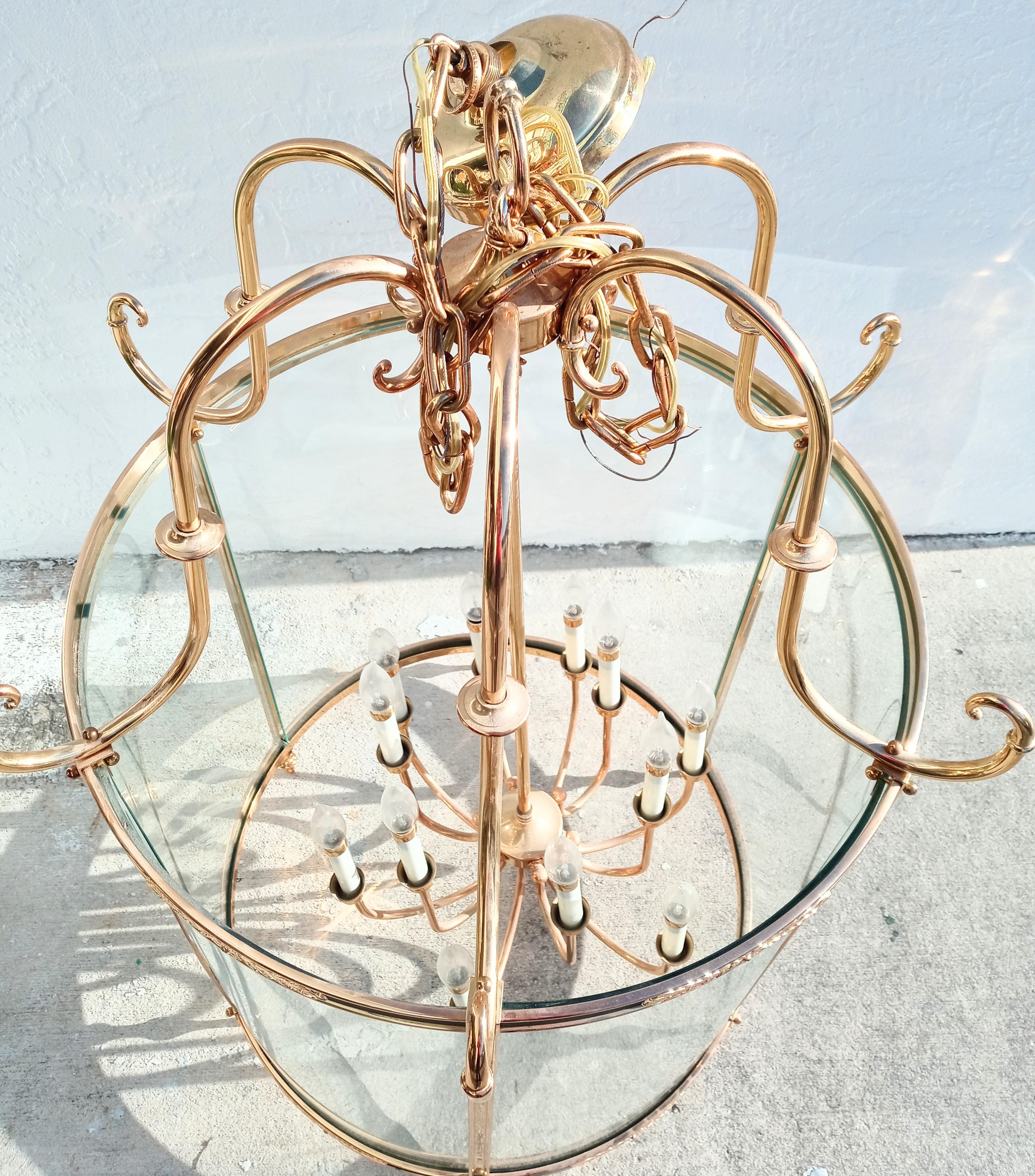 A monumental mansion size solid brass and curved glass cylindrical foyer chandelier.
This light fixture is extremely large with a striking presence.
The photographs truly do not do it justice.
It features 12 candelabra sockets with black accents