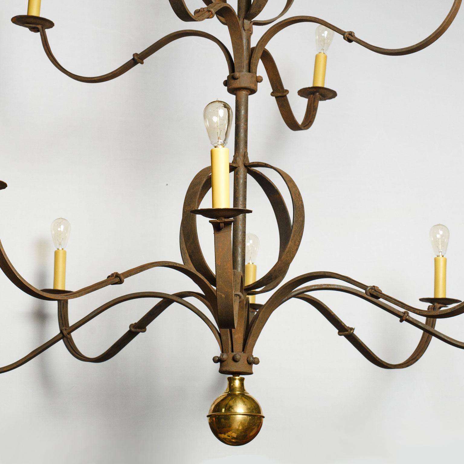 Monumental forged iron chandelier decorated with polished brass finial. Massive iron chandelier hand forged by blacksmith. Its attractive subtly-aged finish serves as the perfect contrast with its polished brass finial detail. Ten arms (four upper