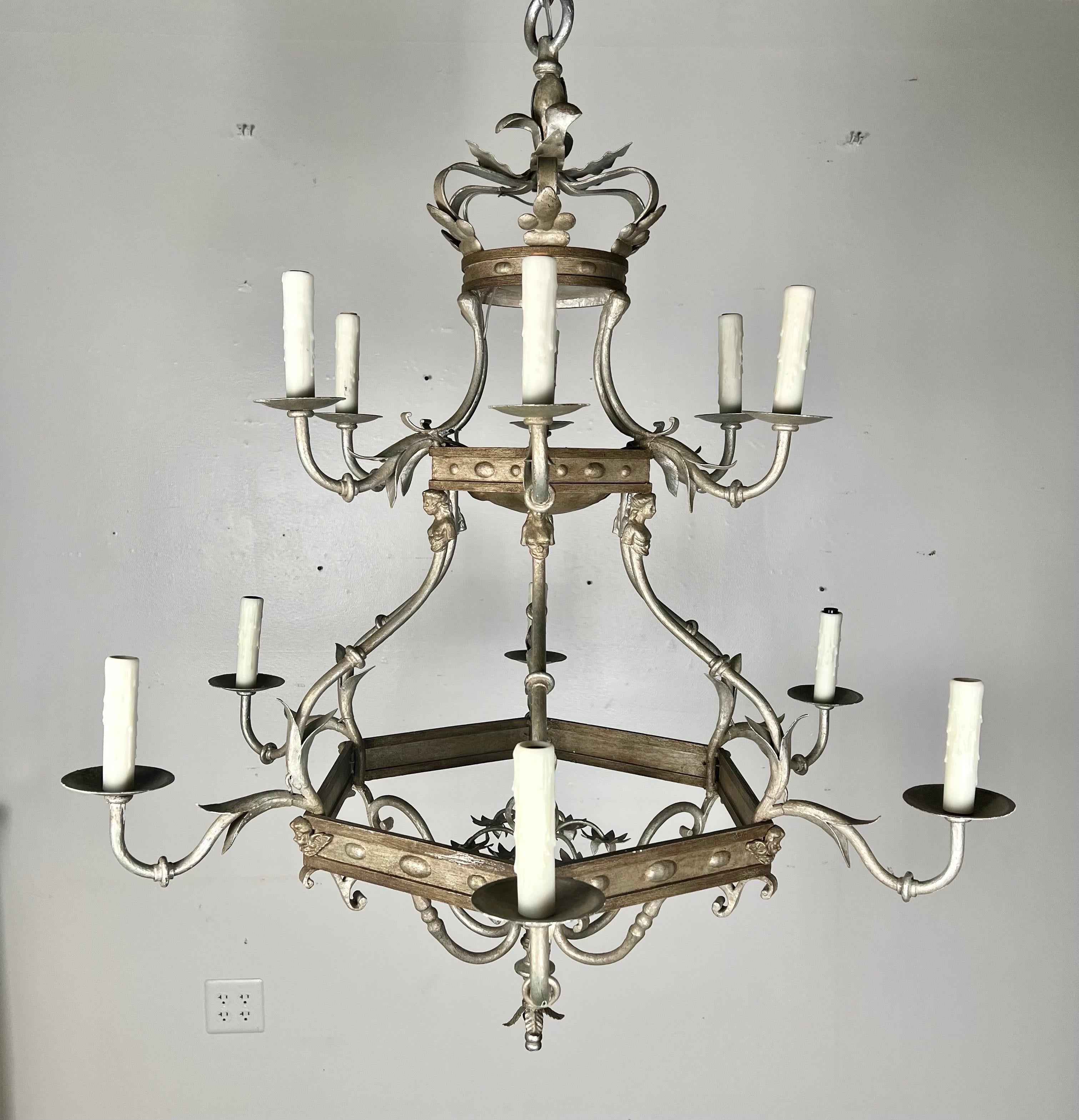 Monumental size 12-light, two-tiered silvered chandelier.  The chandelier is adorned with a crown on top and cherub faces throughout.  The fixture is newly rewired and includes chain & canopy.