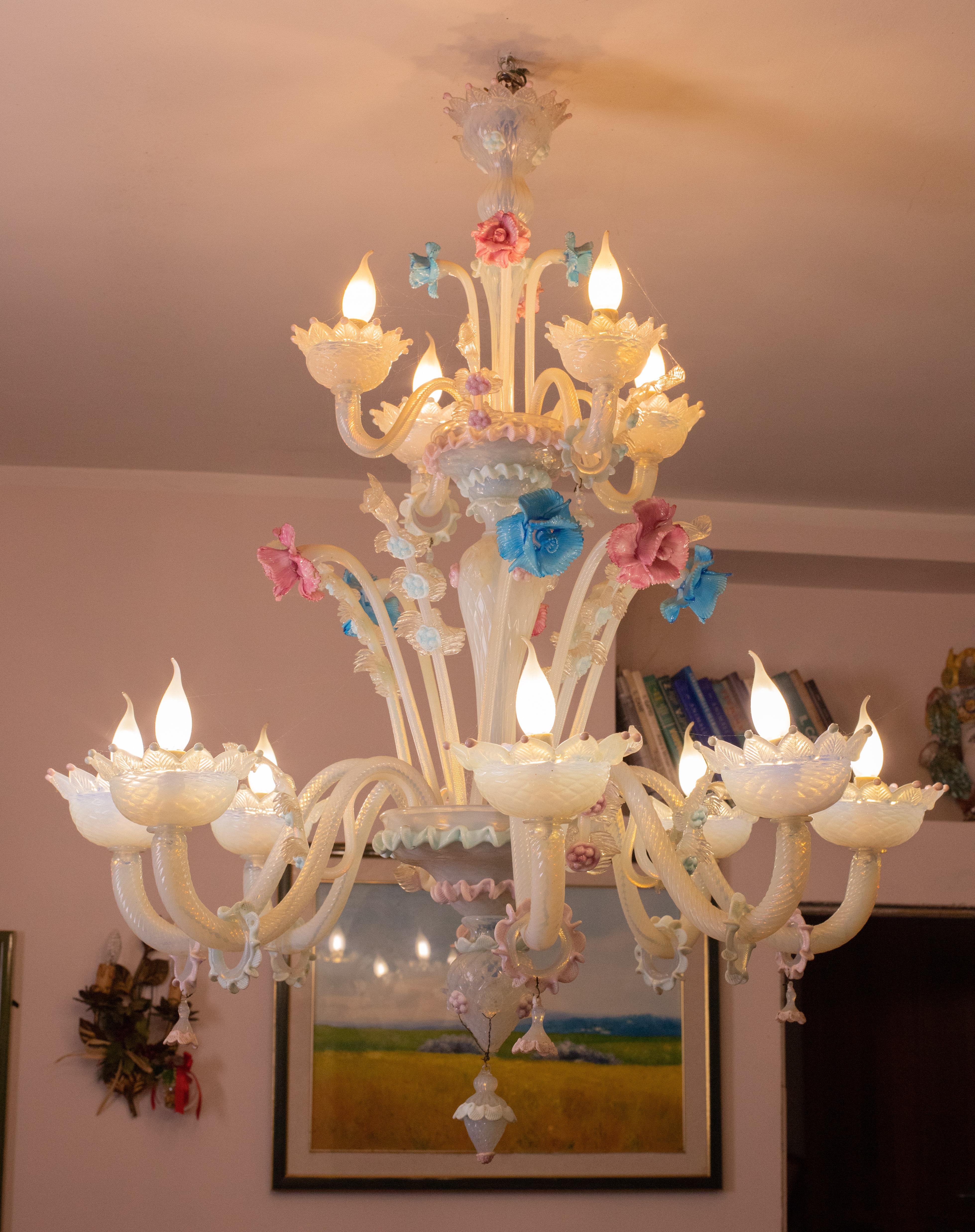 Merveilleux lustre Murano de couleur opaline formé par 12 bras avec 12 points lumineux.

Le lustre est riche en décorations, composé de 12 magnifiques fleurs roses et bleues.

Le lustre convient de préférence aux grands espaces tels que les salons
