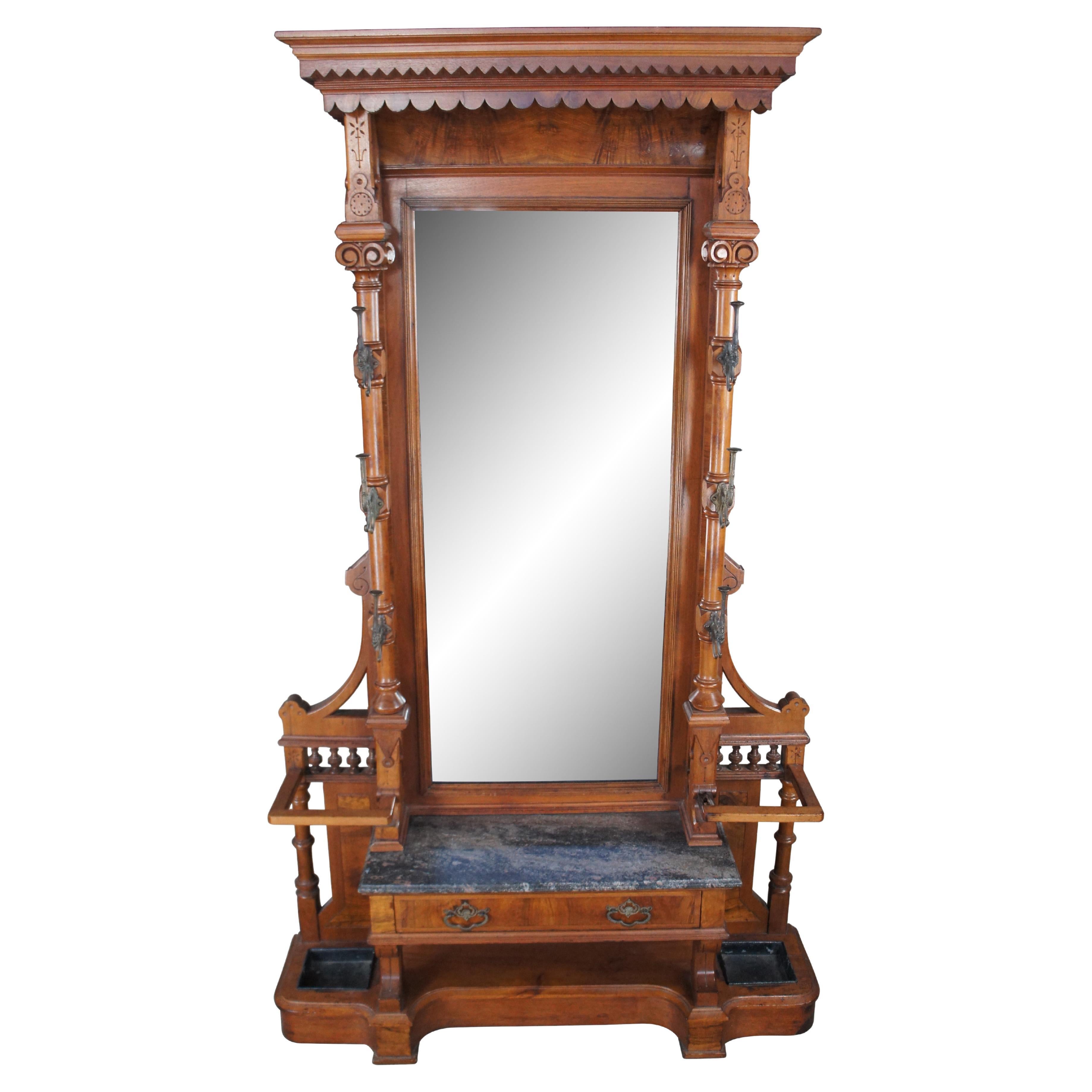 Massive Victorian Era Renaissance Revival hall tree and umbrella stand, circa 1870s.  Made from walnut with a large glass plate pier mirror set between ornately turned columns scrolled along the top with figural double hooks. Beneath the mirror is a
