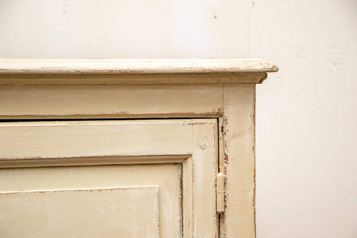 In a pale yellow distressed paint, the interior painted blue-gray. A carved cavetto cornice over double glazed doors on top, opening to four shelves. The separate lower cabinet doors open to two shelves. All doors with French brass escutcheons