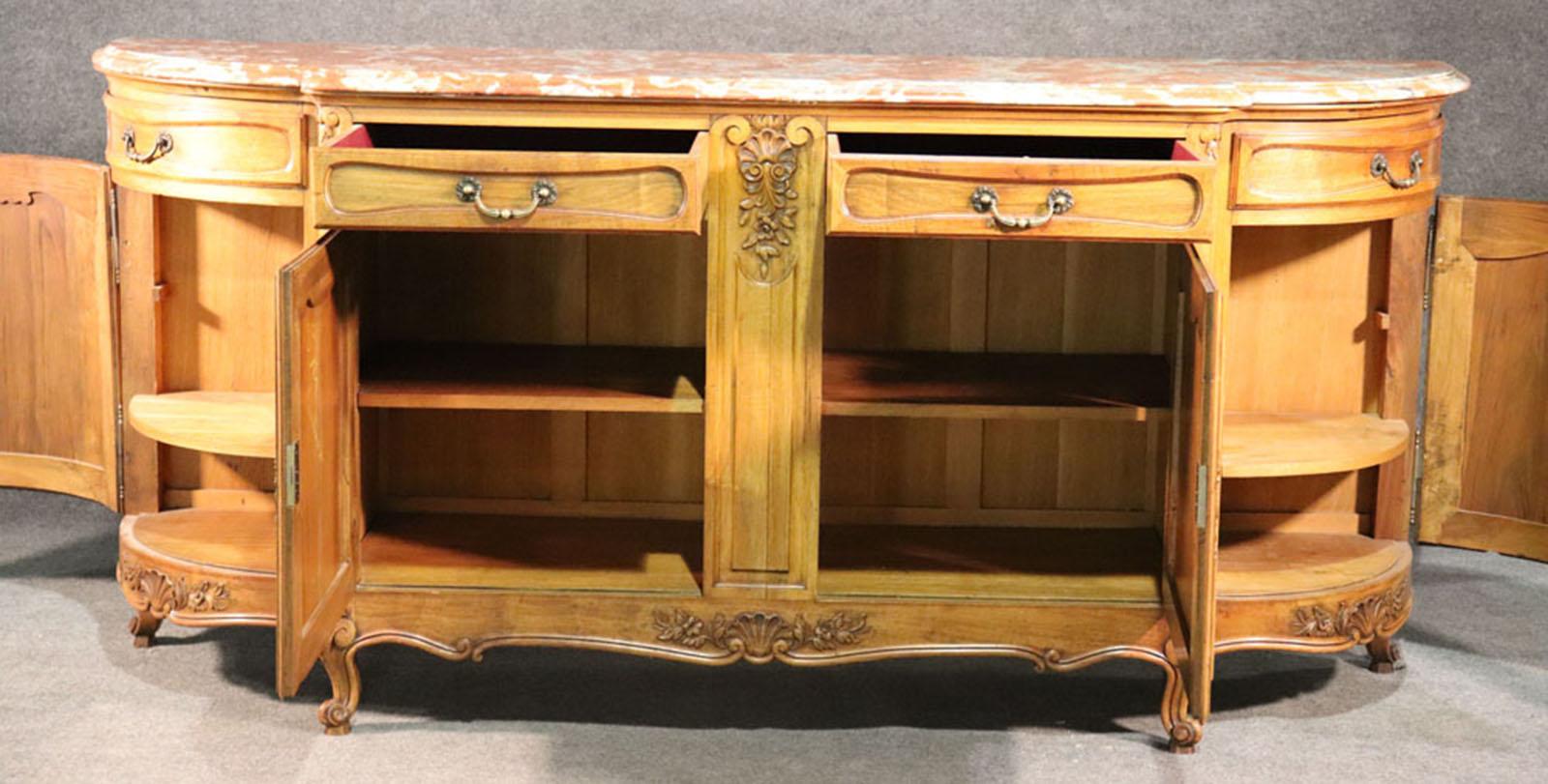 This monumental sideboard features some of the finest carving possible in this style and a gorgeous undamaged slab of marble on top. The marble has hues of coral and whites and is a beautiful contrast to the fruitwood hued walnut case. The piece