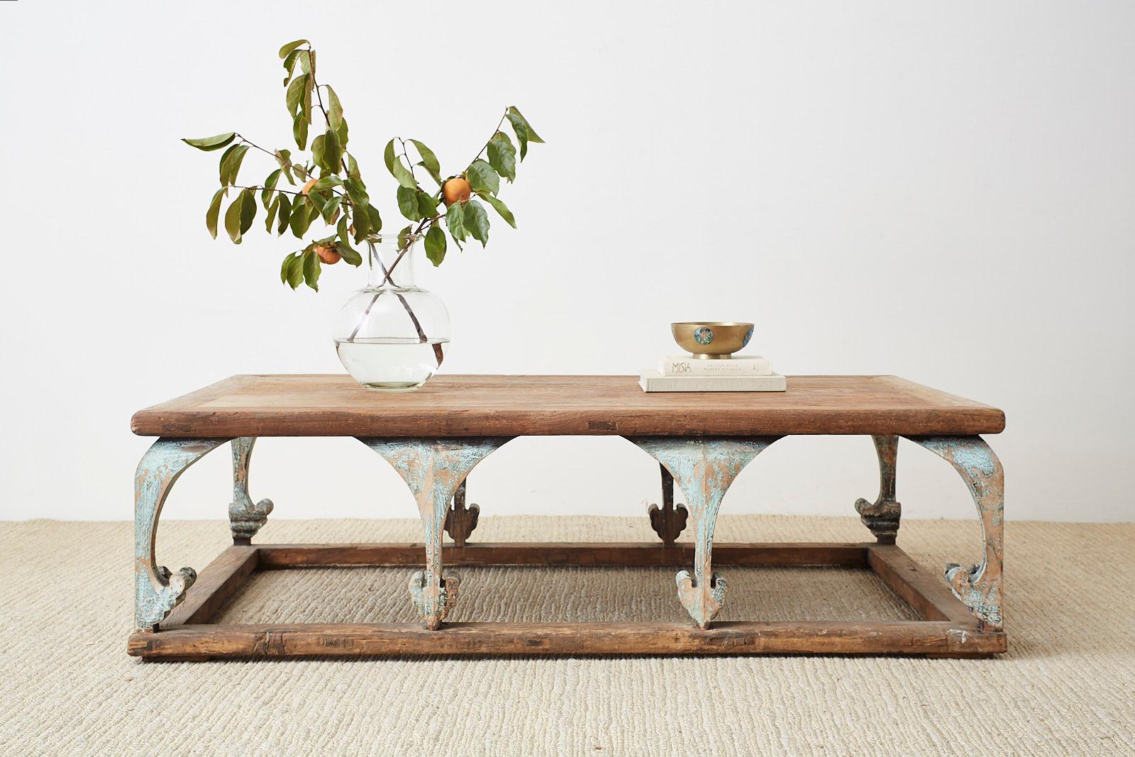 Monumental rectangular coffee or cocktail table having a rustic, weathered patina. Constructed from reclaimed pine featuring arched legs with a spade foot motif. The supports have a distressed polychrome finish with lacquer paint remnants. The aged