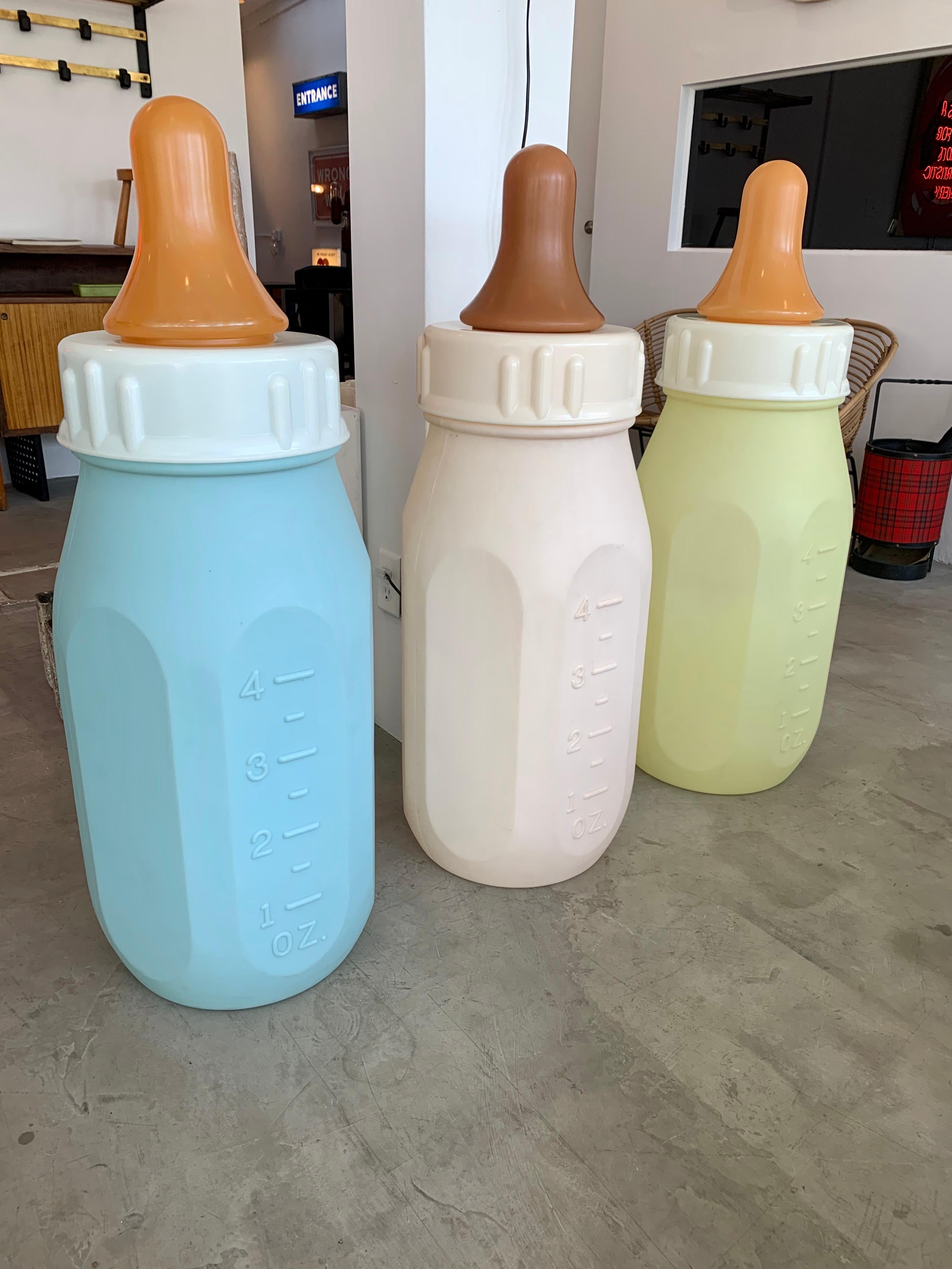 Gigantic baby bottle made in the 1970s. Hard plastic bottle with removable top and rubber nipple. White bottle with ounces on one side and milliliters on the other. At three and a half feet tall and 15