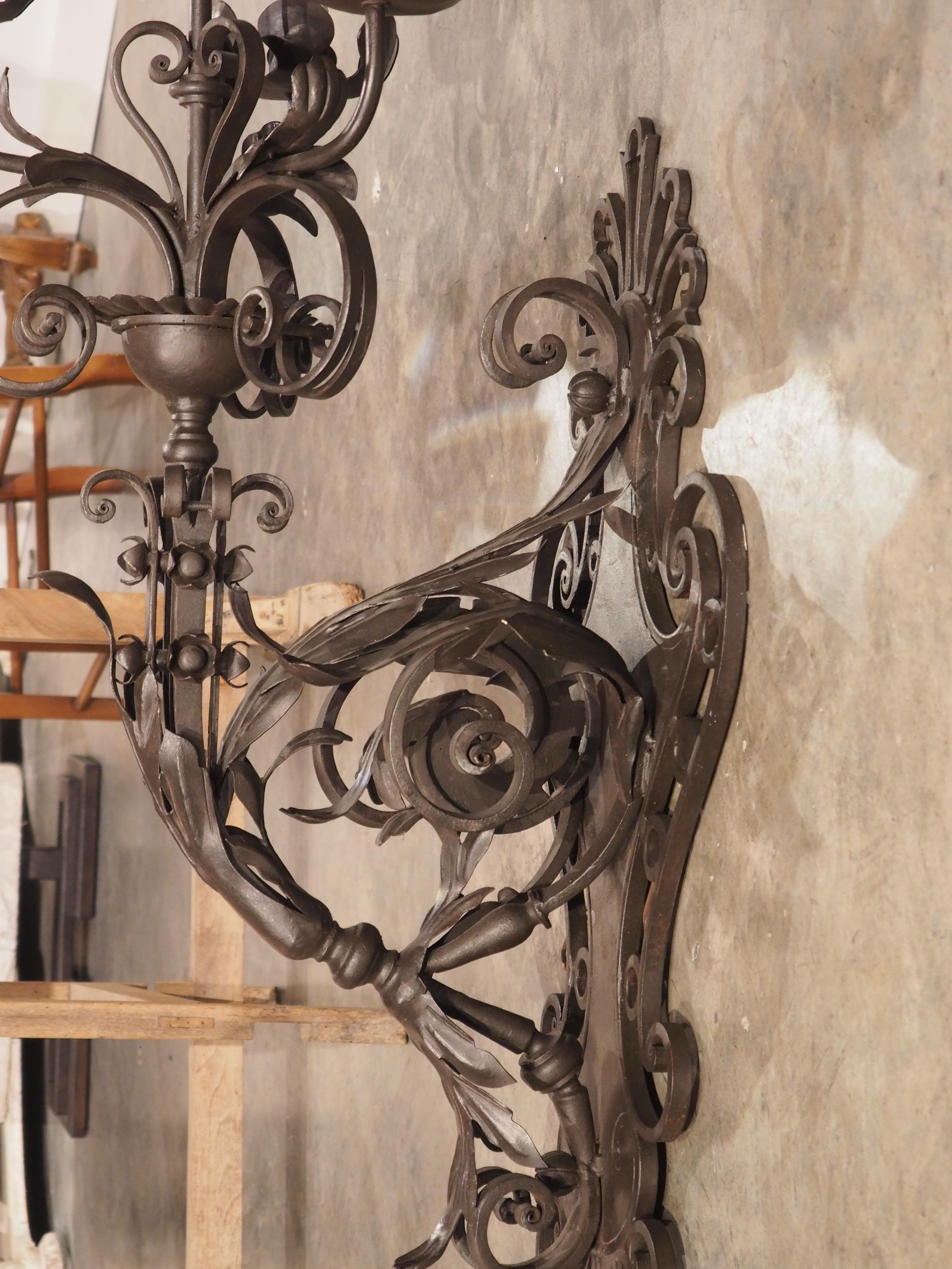 Wrought in the style of Spanish architectural lighting, this monumental iron four-light wall sconce is topped by white faux candle sleeves rising from saucer large, parted leaf bobeches atop gently curving arms. One light rises above the other three