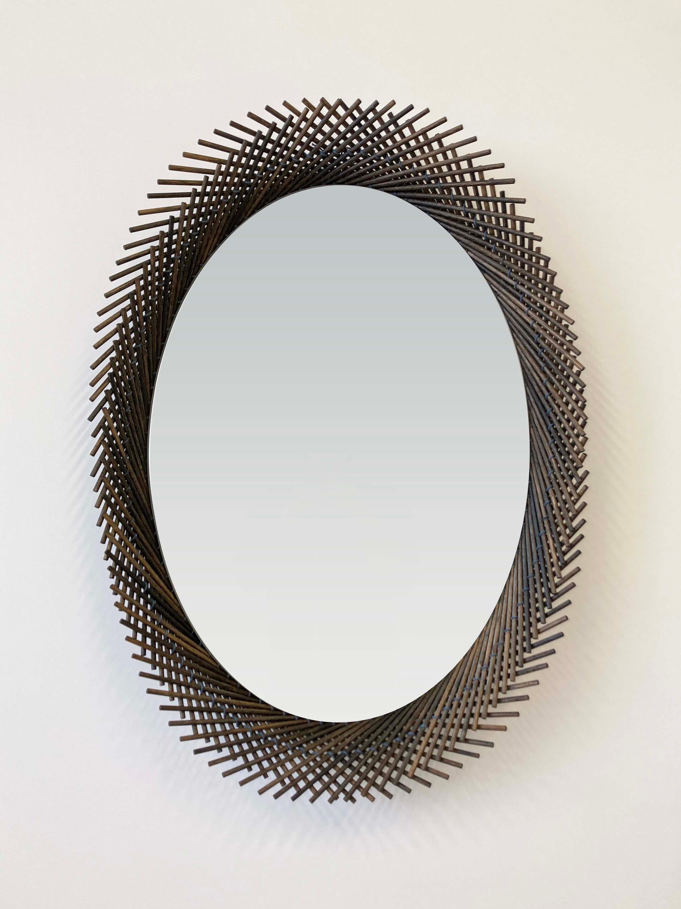 The Mooda Oval Mirror pushes the strict geometry that occurs as a result of stitching the dowels together to create a dynamic edge. Each layer of the Mooda rises and falls inversely to the other as they travel along the circumference of the mirror,