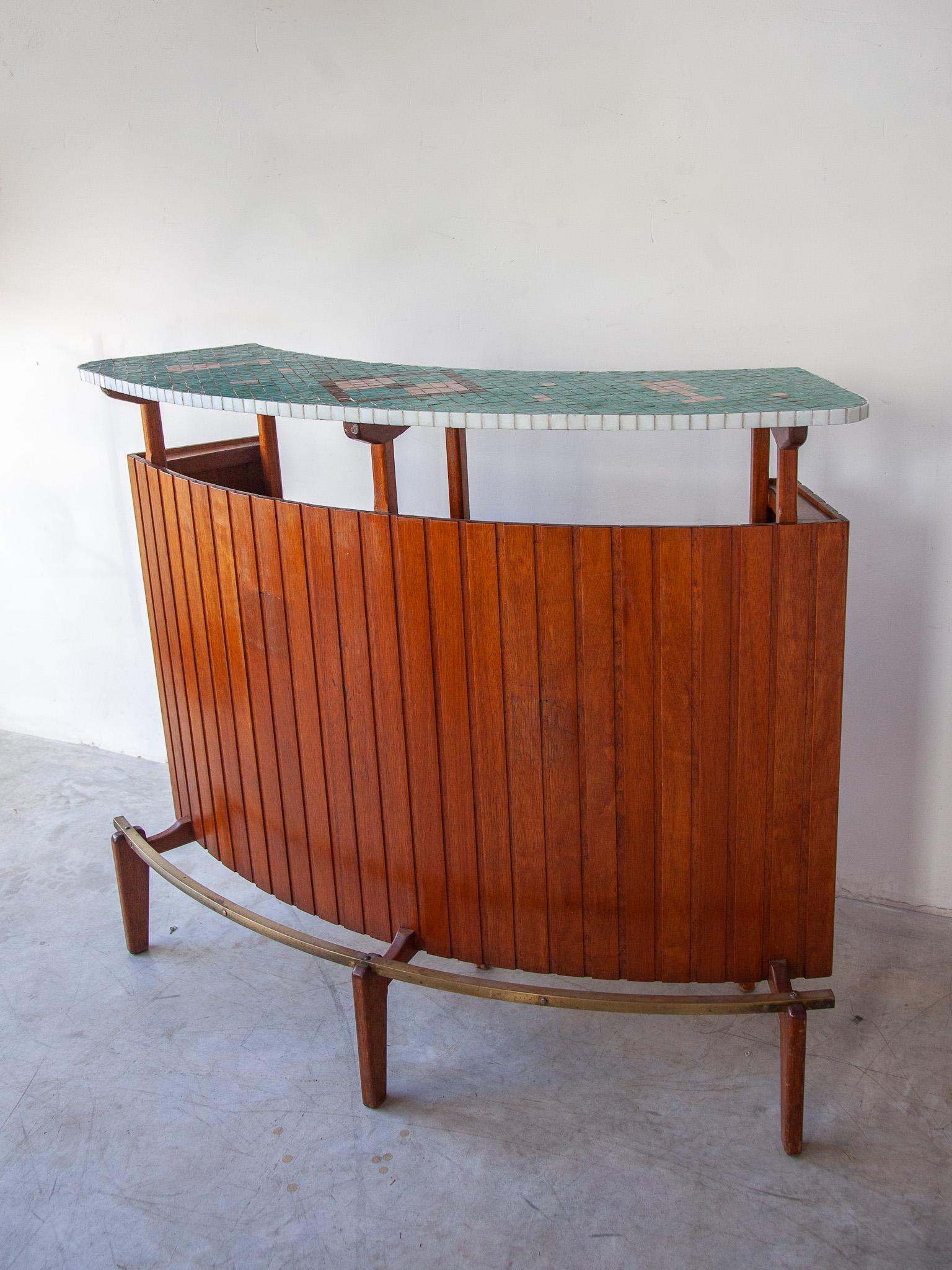 Vintage counter bar in solid teak with ceramic mosaic top and brass footrest. The design drink bar has a rounded shape and a front covered with solid teak slats.

Ideally placed in a corner, off your living room or office even a beautiful piece