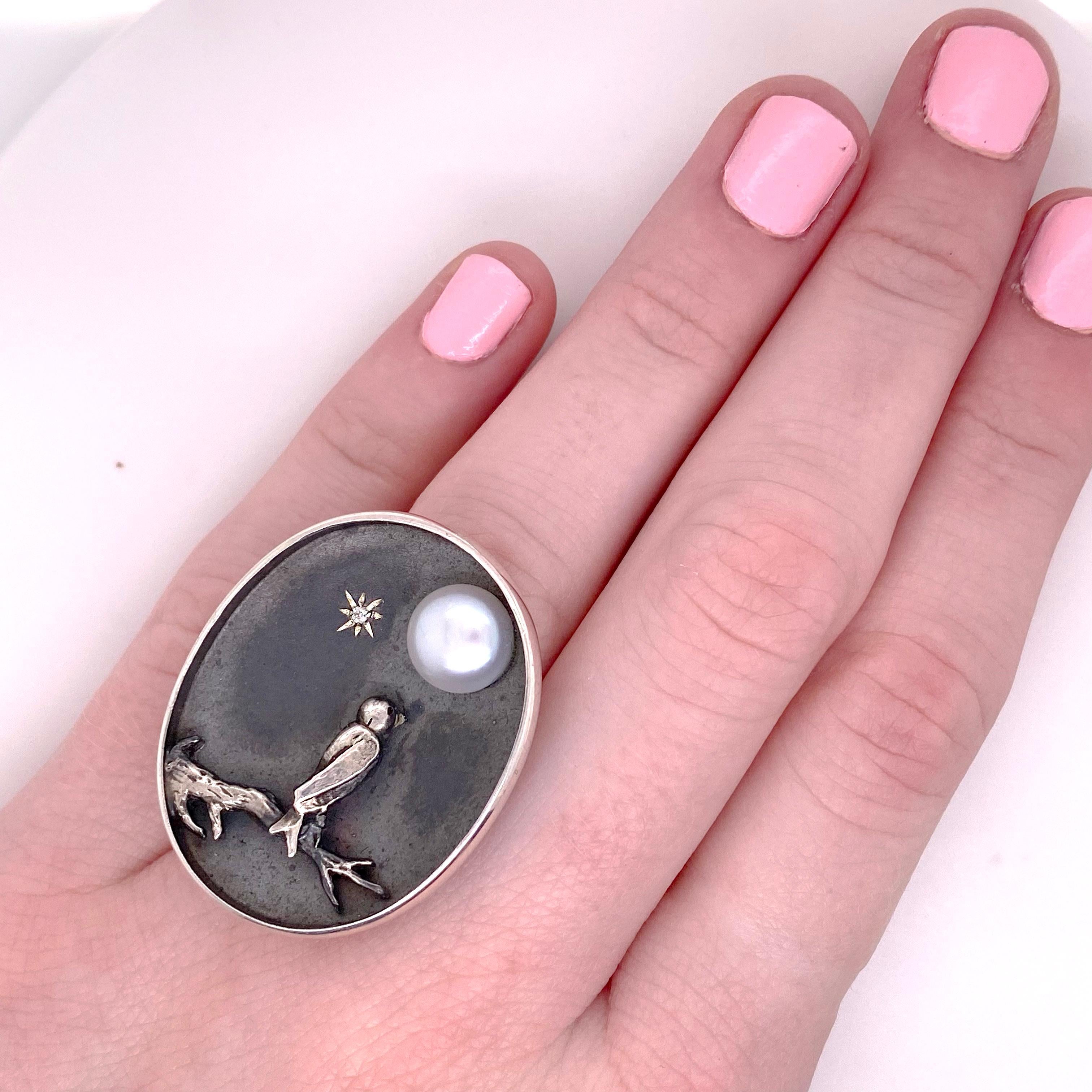 By the Moonlight features a raised silver tree branch with a bird looking up to the Pearl Moon. The gorgeous oval shape with the black oxidation background makes the silver branch and bird really pop.  There is a sparkle for the North Star and a