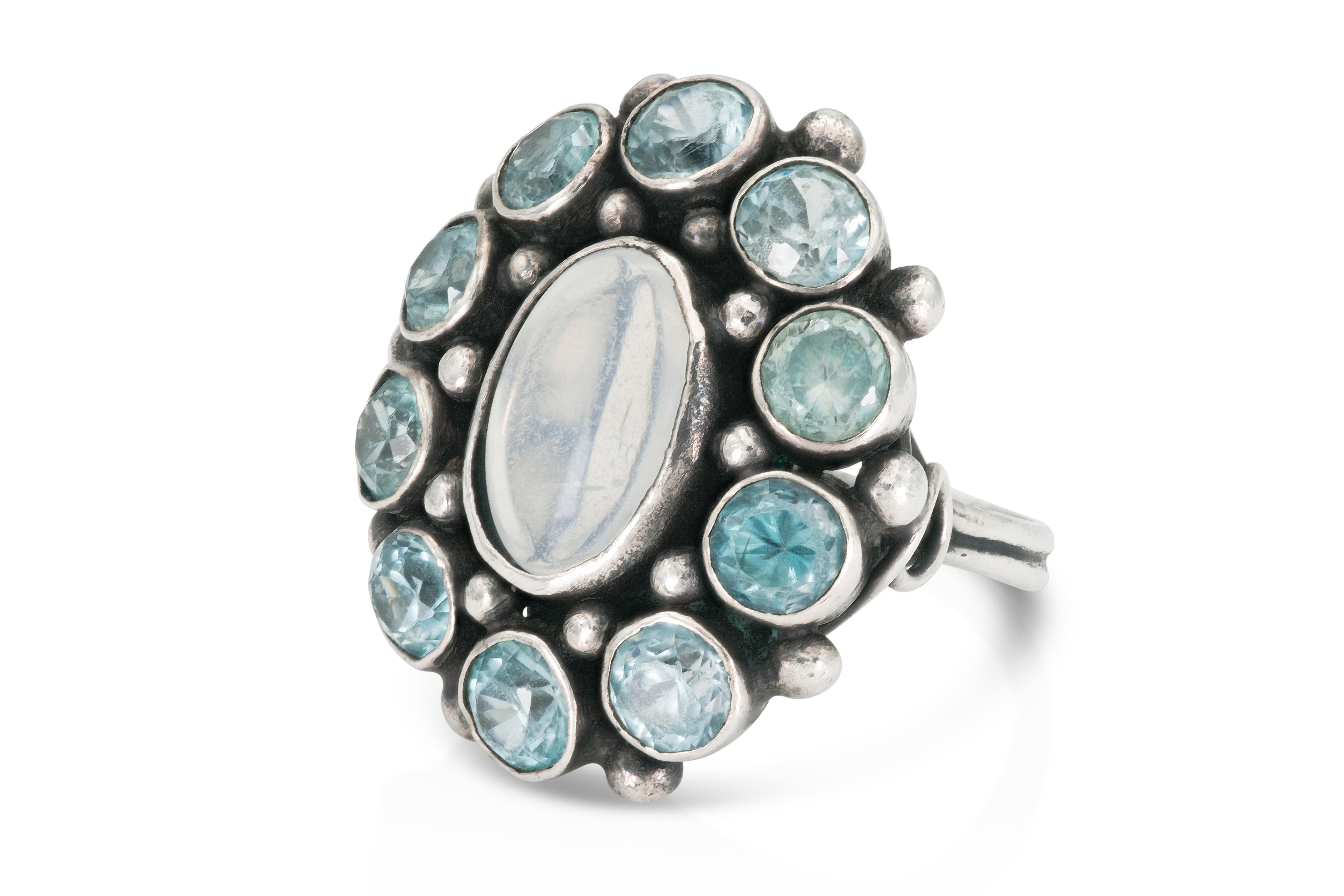 Fein gearbeiteter Silberschmuck mit einem Mondstein in der Mitte und blauen Zirkonen im Rundschliff.
Größe 5 1/2, größenverstellbar