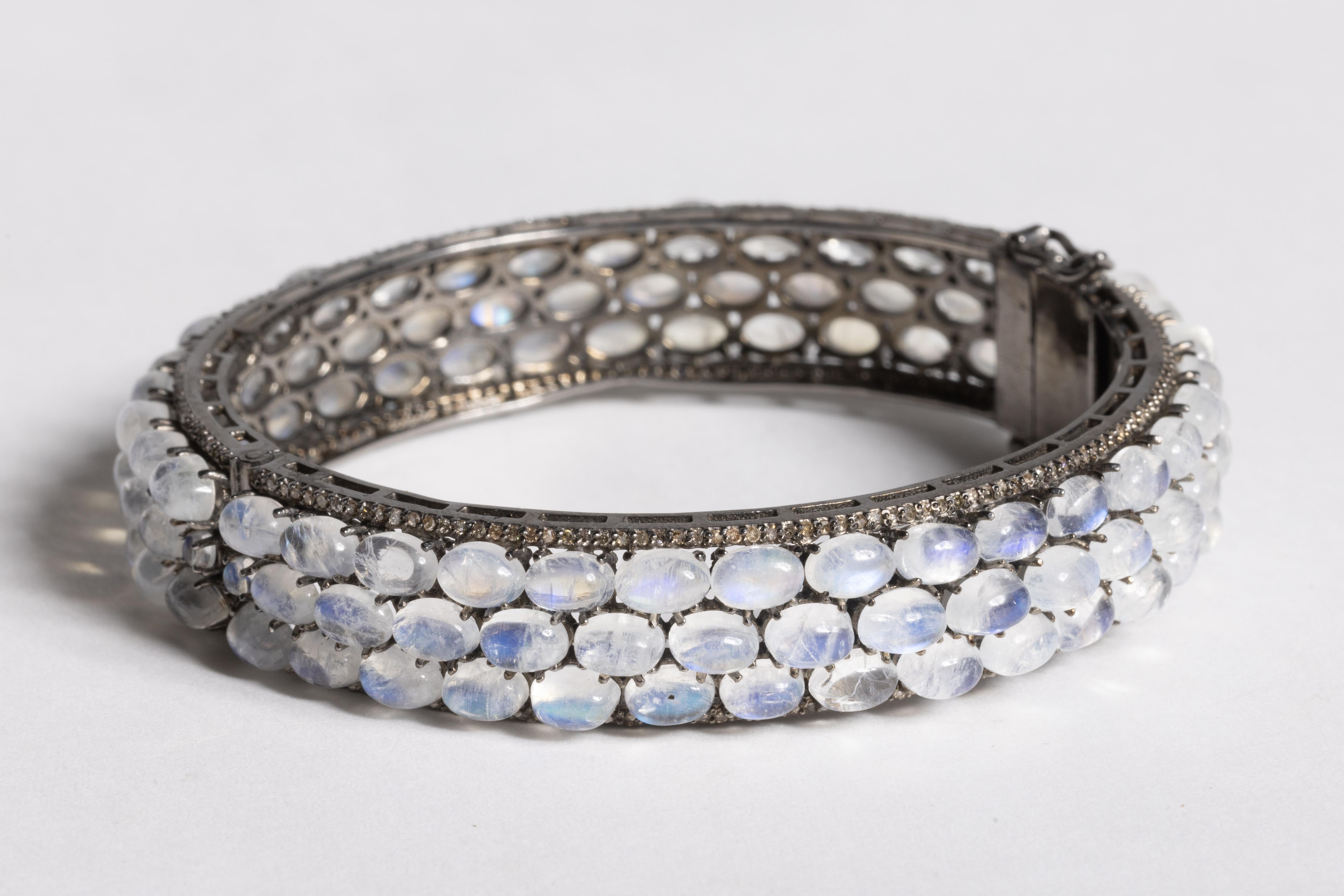 Superbe bracelet à charnière composé de trois rangées de pierres de lune ovales en cabochon, bordées de diamants ronds de taille brillant.  Serti dans un boîtier en argent sterling oxydé.  Fermoir à poussoir avec deux sécurités.  La circonférence