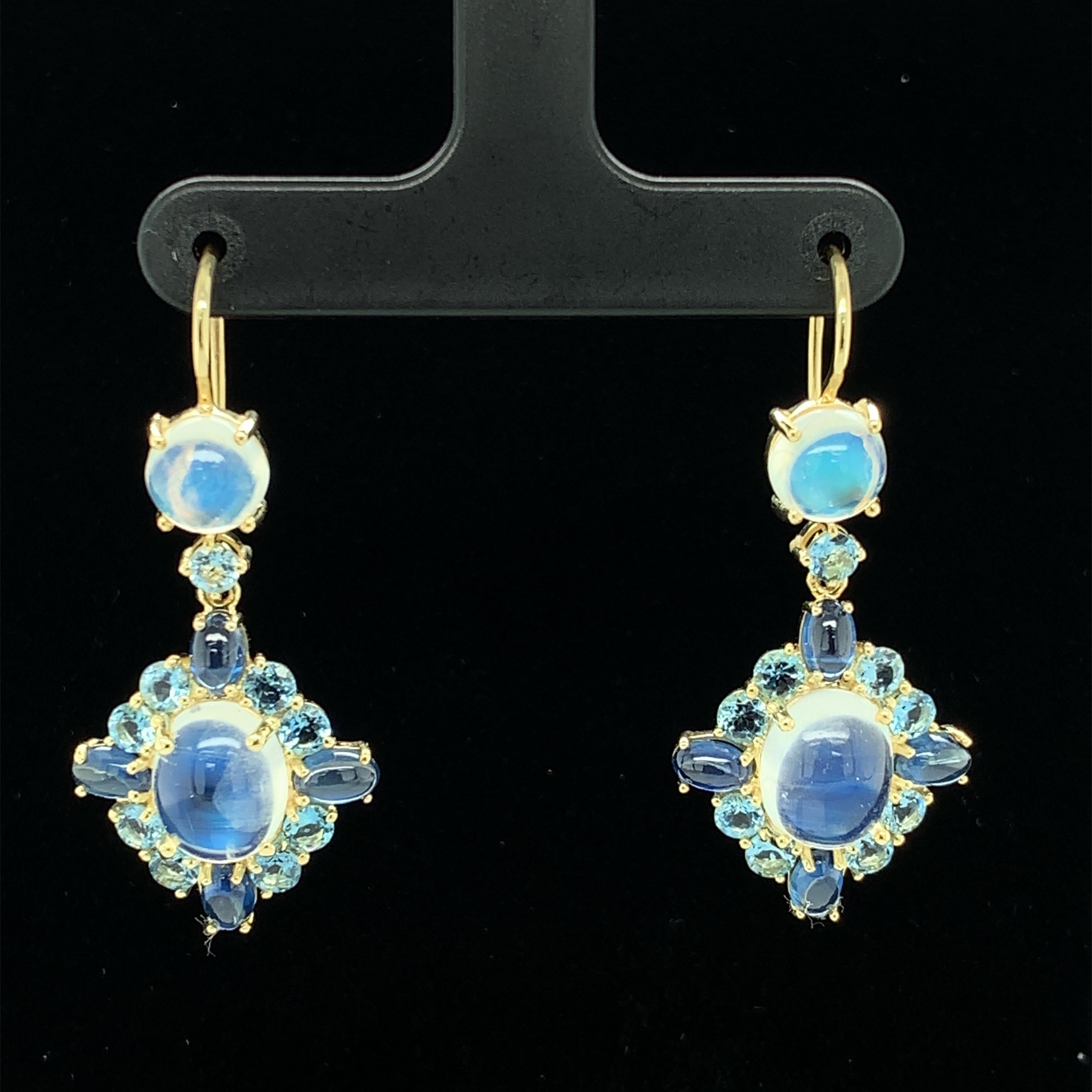 Designed to be as fun as they are elegant, these handmade 18k yellow gold drop earrings feature quality craftsmanship and a striking combination of “blue flash” moonstones, rich blue sapphire cabochons, and faceted aquamarines of unusually deep