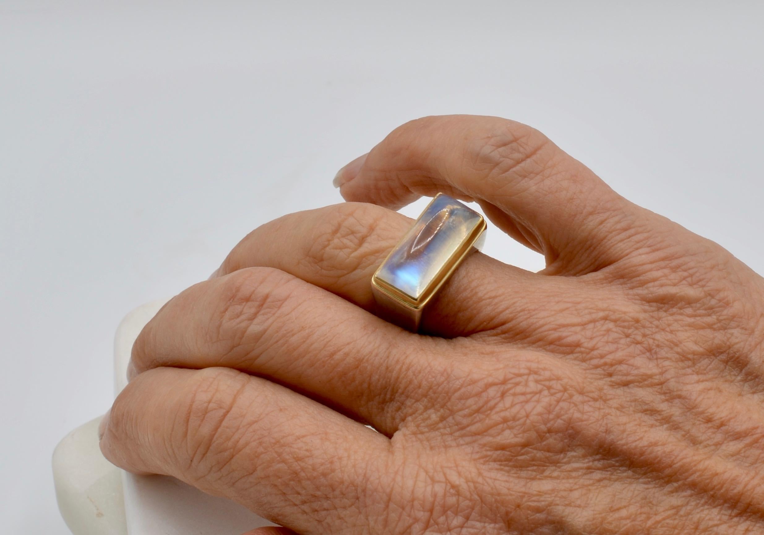 This rectangle  Steven Battelle designed moonstone ring is cut to reflect the rainbow of the moonstone beautifully. It is accented by a 18 karat yellow bezel and set in a modern chunky sterling silver setting. The ring style is masculine and the