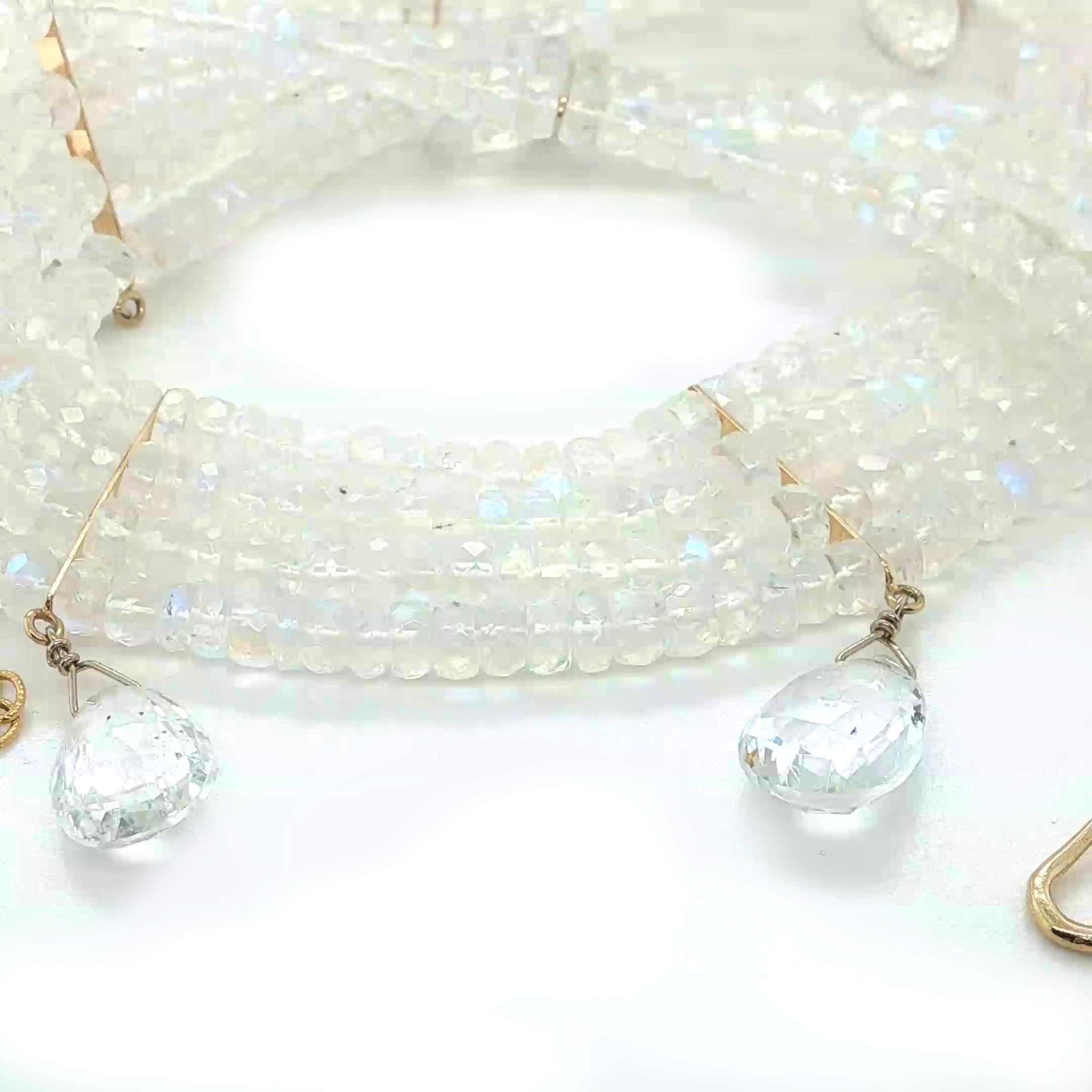 Questa splendida collana a più fili presenta quattro fili di perle di pietra di luna arcobaleno splendidamente sfaccettate e splendide gocce di topazio cristallino briolette accentate con oro giallo 14k. Le pietre di luna hanno una sottile