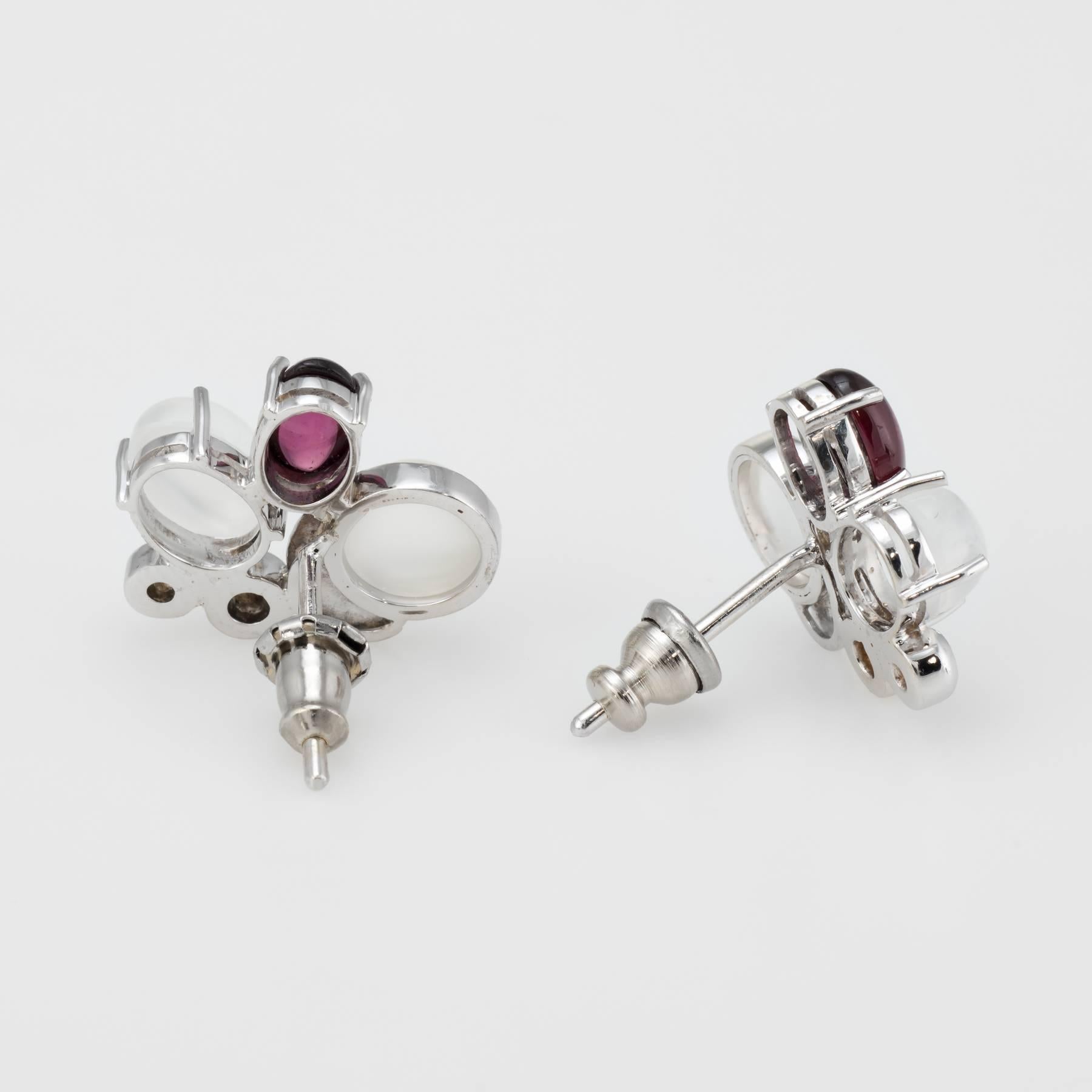 Elegant pair of gemstone cluster earrings, crafted in 14k white gold. 

Moonstone measures 7mm x 5mm and 6mm (3.50 carats total estimated weight), accented with 6mm x 4mm cabochon cut rhodolite garnets (estimated at 0.80 carats). The diamonds total