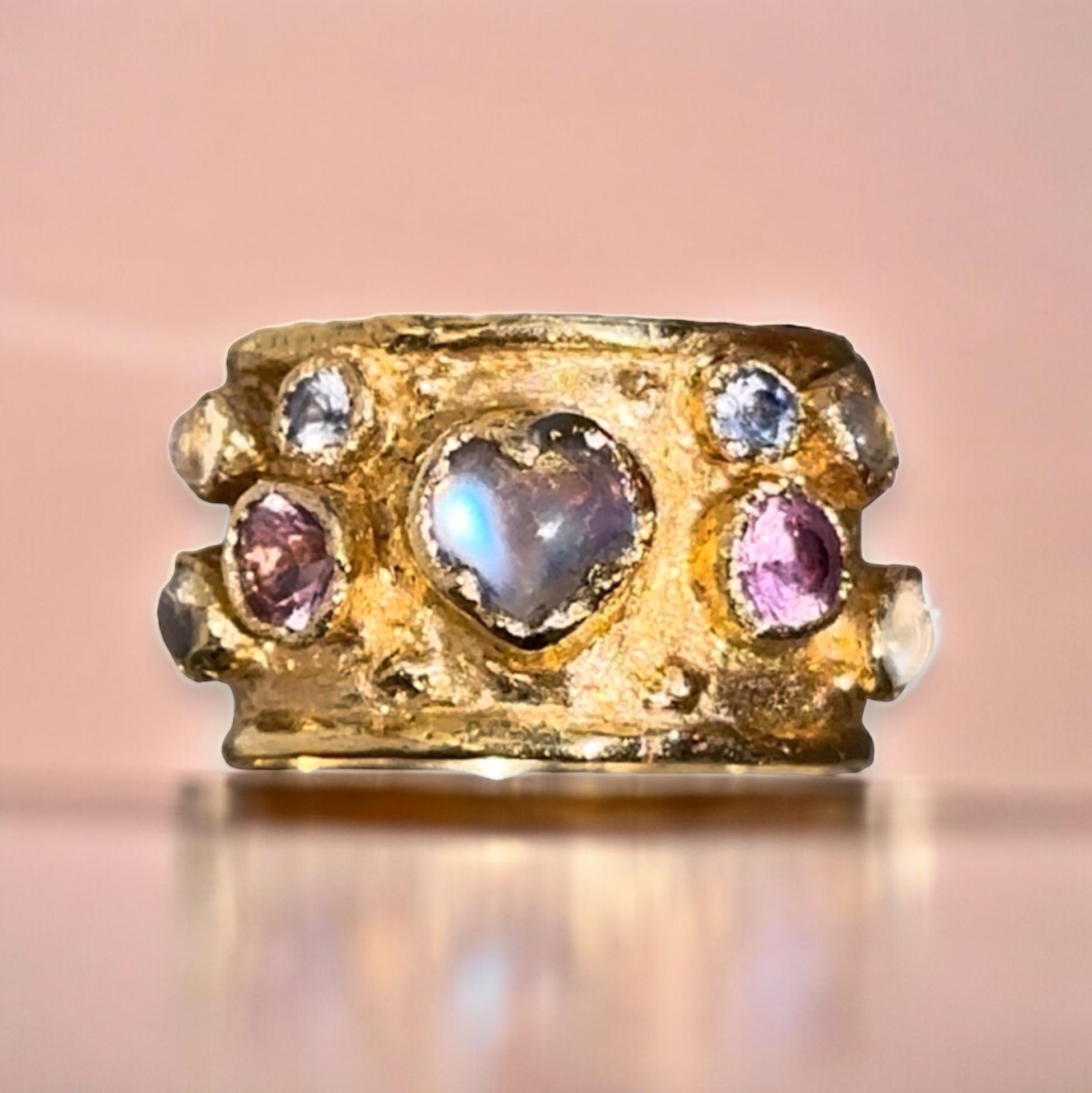 Introducing a unique 18 Ct Gold handcrafted cigar ring featuring a stunning Blue moonstone heart that radiates a captivating glow, beautifully accented by sapphires and moonstones. This exquisite piece blends slight rococo influences with a modern