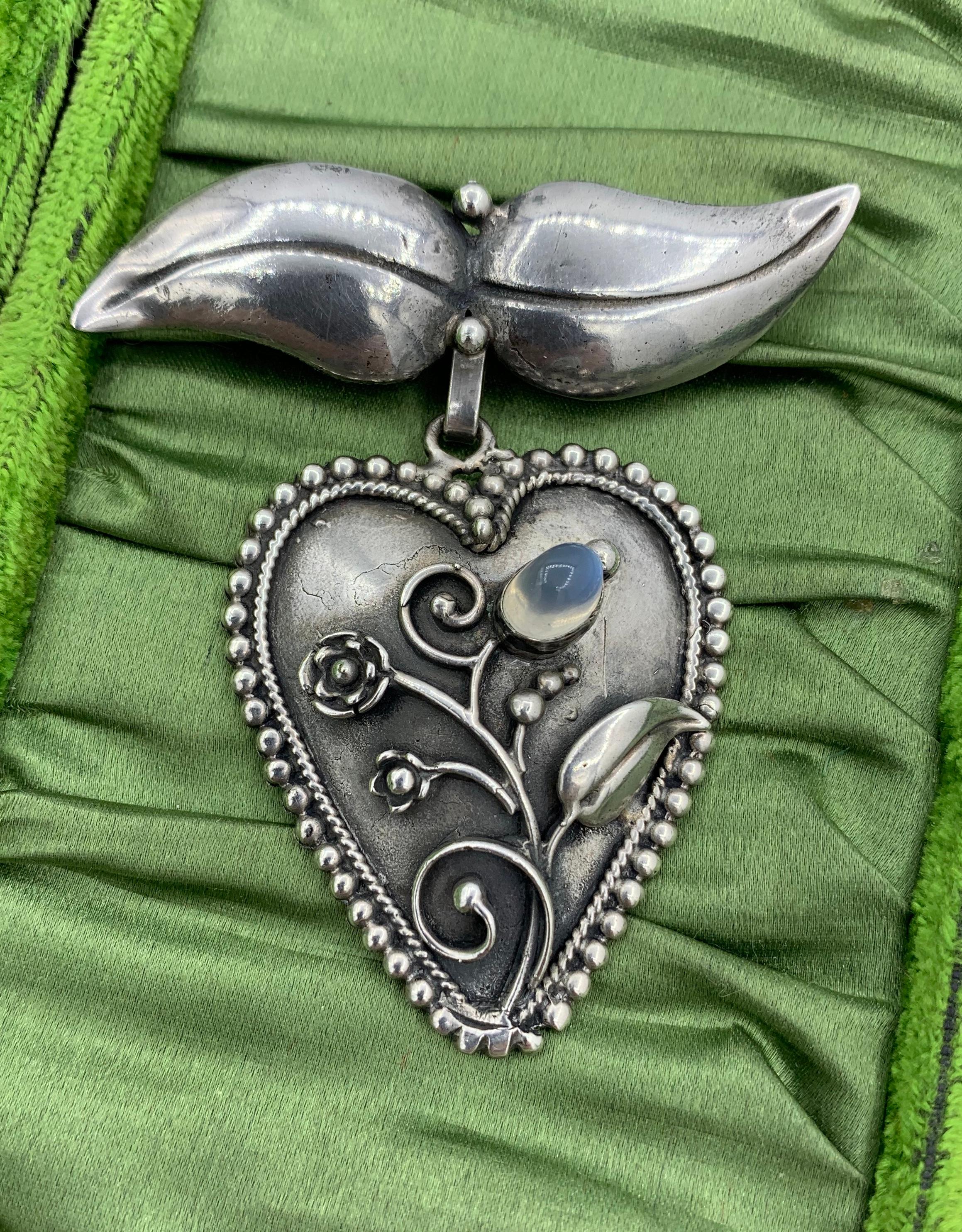 This is a stunning heart shaped brooch pendant pin with an applied design in Sterling Silver of a flower and leaf motif with a moonstone cabochon.  The heart has a lovely beaded border.  The heart can be removed from the leaf form top portion.  The