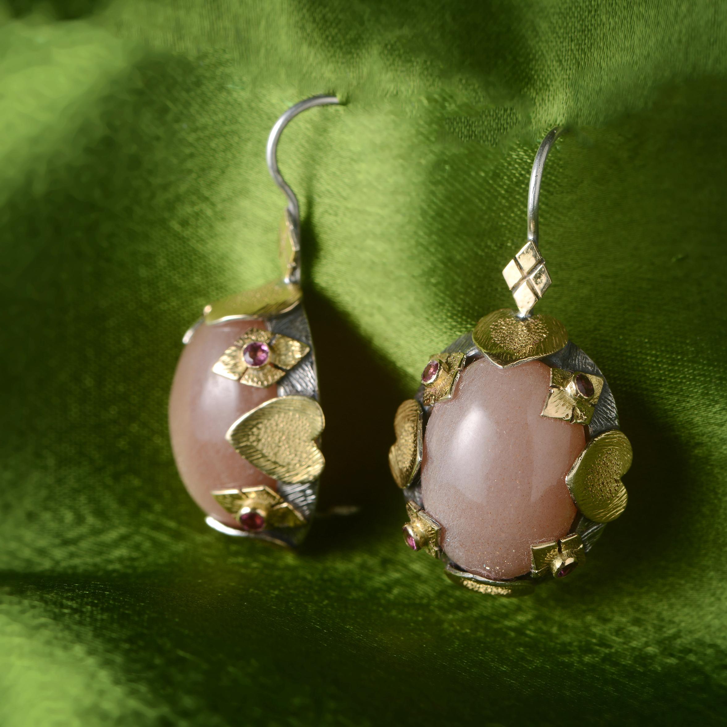 These gorgeous moonstone tourmaline earrings are one of a kind.

Handmade in our workshops they have chocolate moonstone drops, which are surrounded by pink tourmalines. We have used hand engraved 18ct gold and overlaid it onto oxidized silver. The
