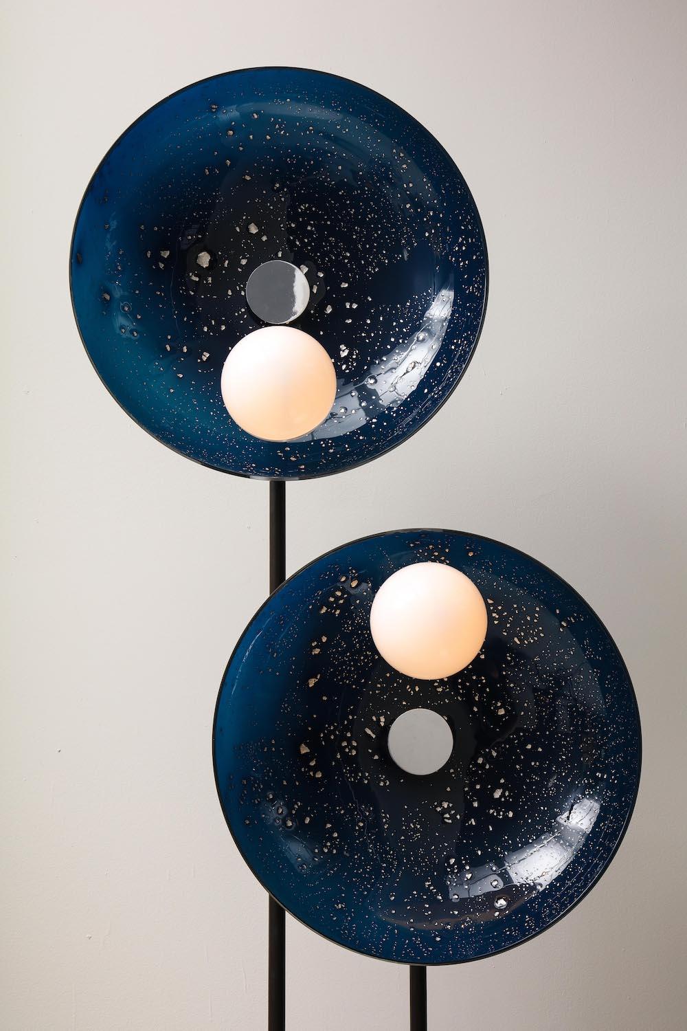 Two shallow glass bowls in ultramarine blue, with applied platinum foil, and two glass-globe shades. Each globe is half opaque-white and half clear. All glass is hand-blown by the artist. Black-patinated bent brass arm with chrome-plated mounts.
