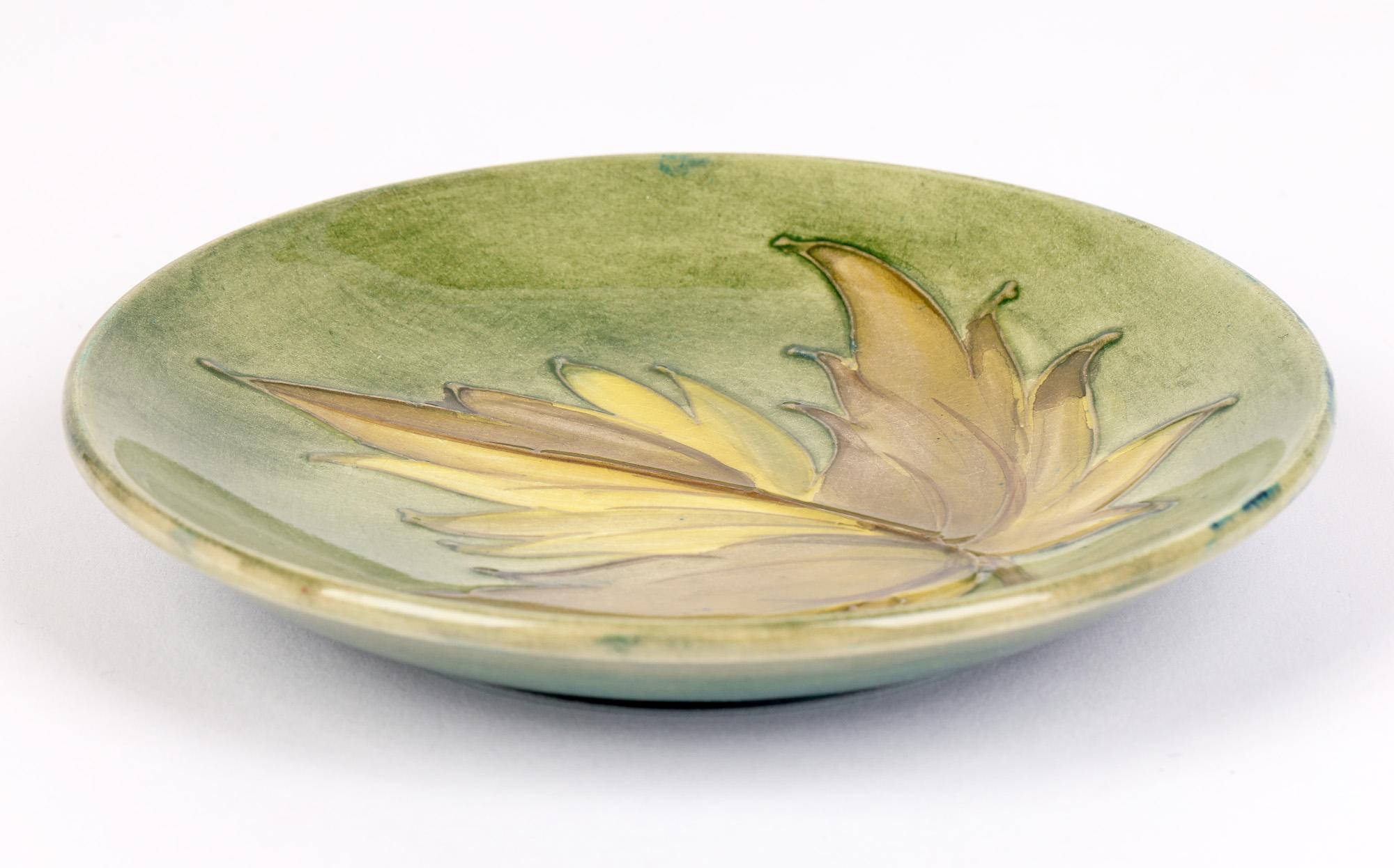A finely made Art Deco Moorcroft tubelined pin dish decorated with a leaf dating from around 1930. The ceramic dish is of simple round shape with a raised edge and stands raised on a narrow round foot. The dish is decorated with a tubelined leaf