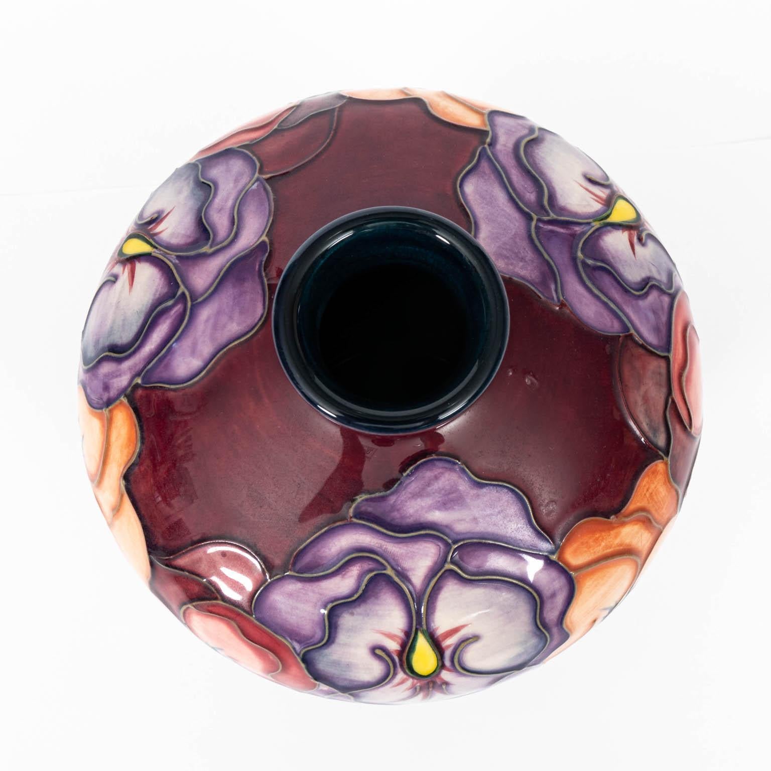 Modern pansy design vase with burgundy background and floral design of various colored pansies circa 1990s. This vase is hand made and hand painted. The vase is marked on the base Moorcroft. Made in England, WM. Please note of wear consistent with