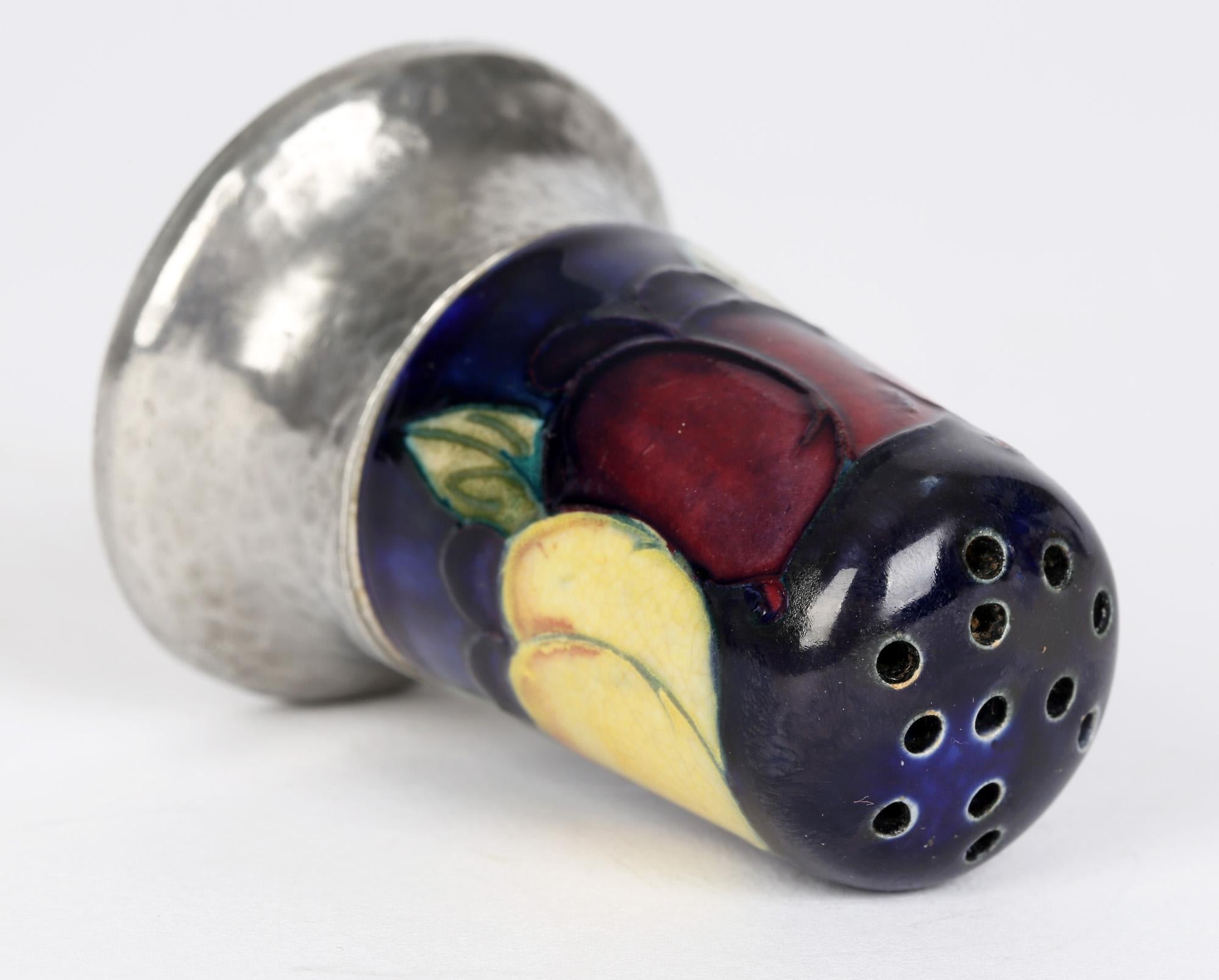 A scarce and unusual Moorcroft Wisteria pattern pepperette with a Tudric planished pewter base dating from around 1920. The pepperette body is of simple thimble shape with tube lined fruit like designs hand painted in tones of red, blue, yellow and
