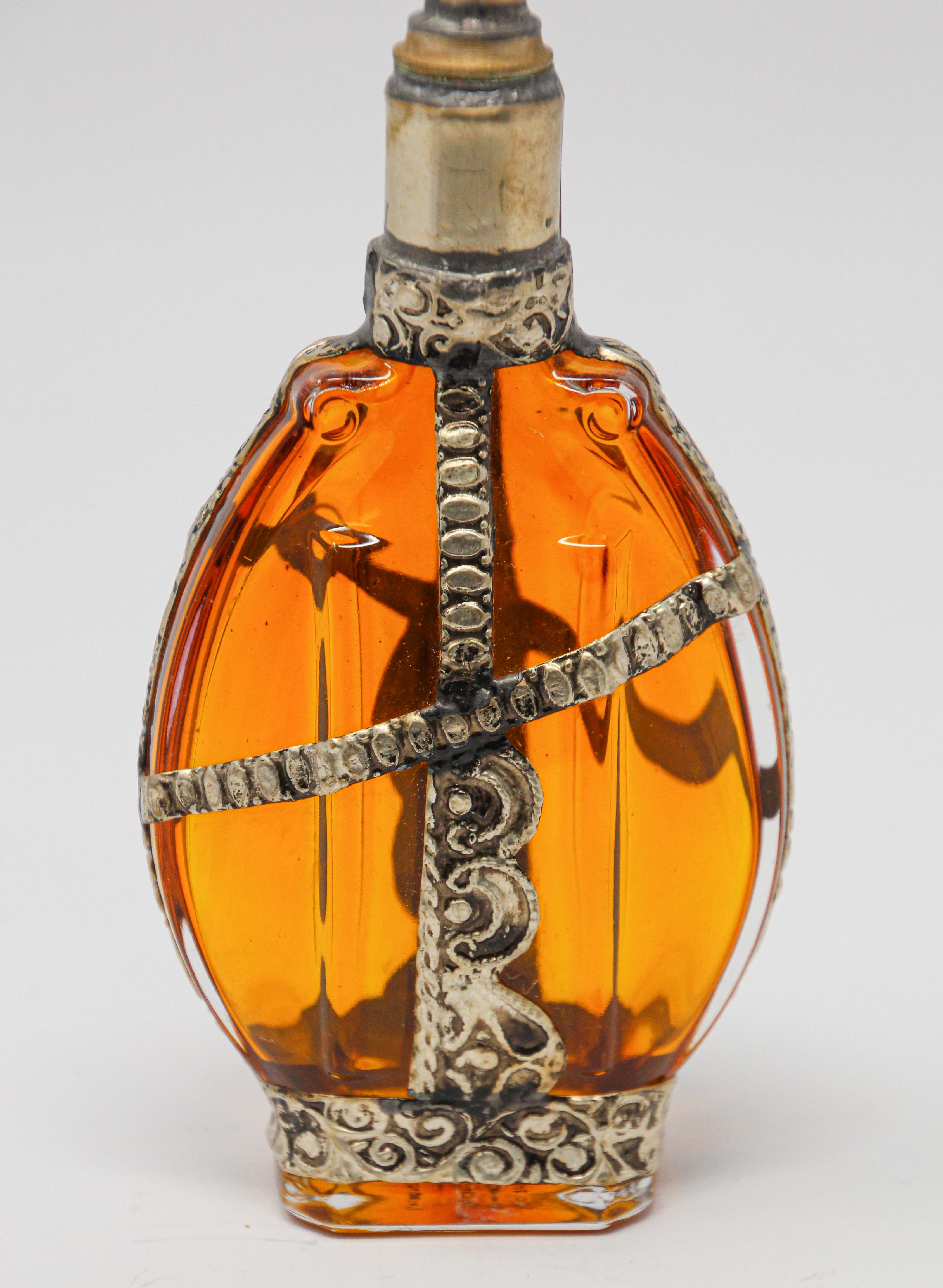 Handcrafted Moroccan Moorish amber painted glass perfume bottle or rose water sprinkler with raised embossed silvered metal floral design over amber glass.
The pressed glass bottle in Art Deco, Art Nouveau style is oval shape with curved sides and