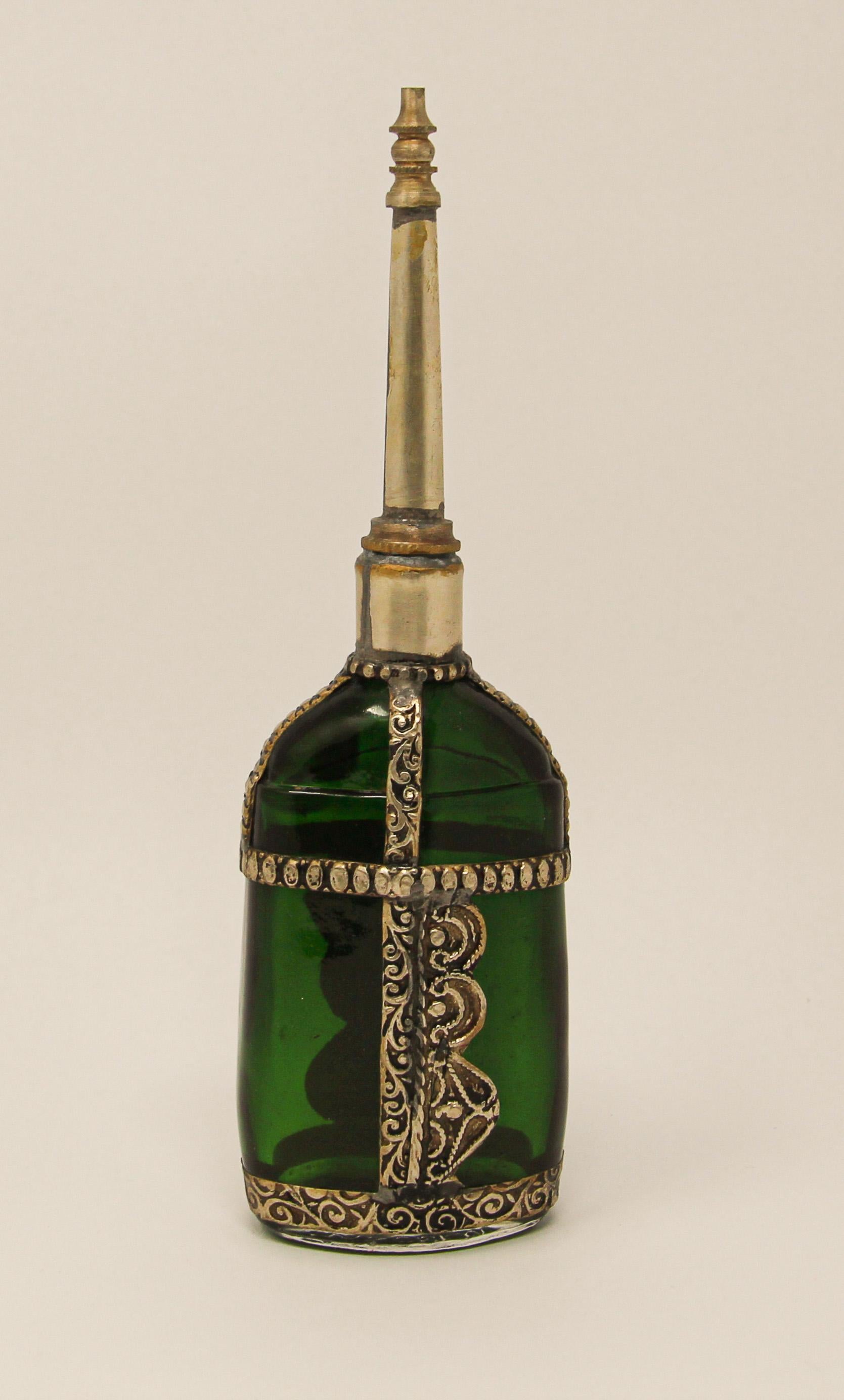 Handcrafted Moroccan Moorish green glass perfume bottle or rose water sprinkler with raised embossed silvered metal floral design over glass.
The pressed glass bottle in Art Deco, Art Nouveau style is oval shape with curved sides and hand decorated