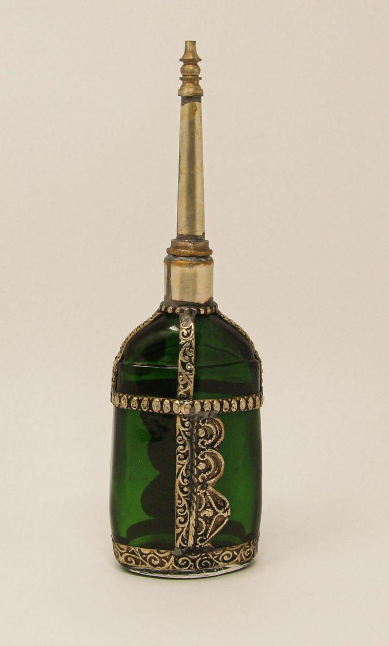 Handcrafted Moroccan Moorish green painted glass perfume bottle or rose water sprinkler with raised embossed silvered metal floral design over glass.
The pressed glass bottle in Art Deco, Art Nouveau style is oval shape with curved sides and hand