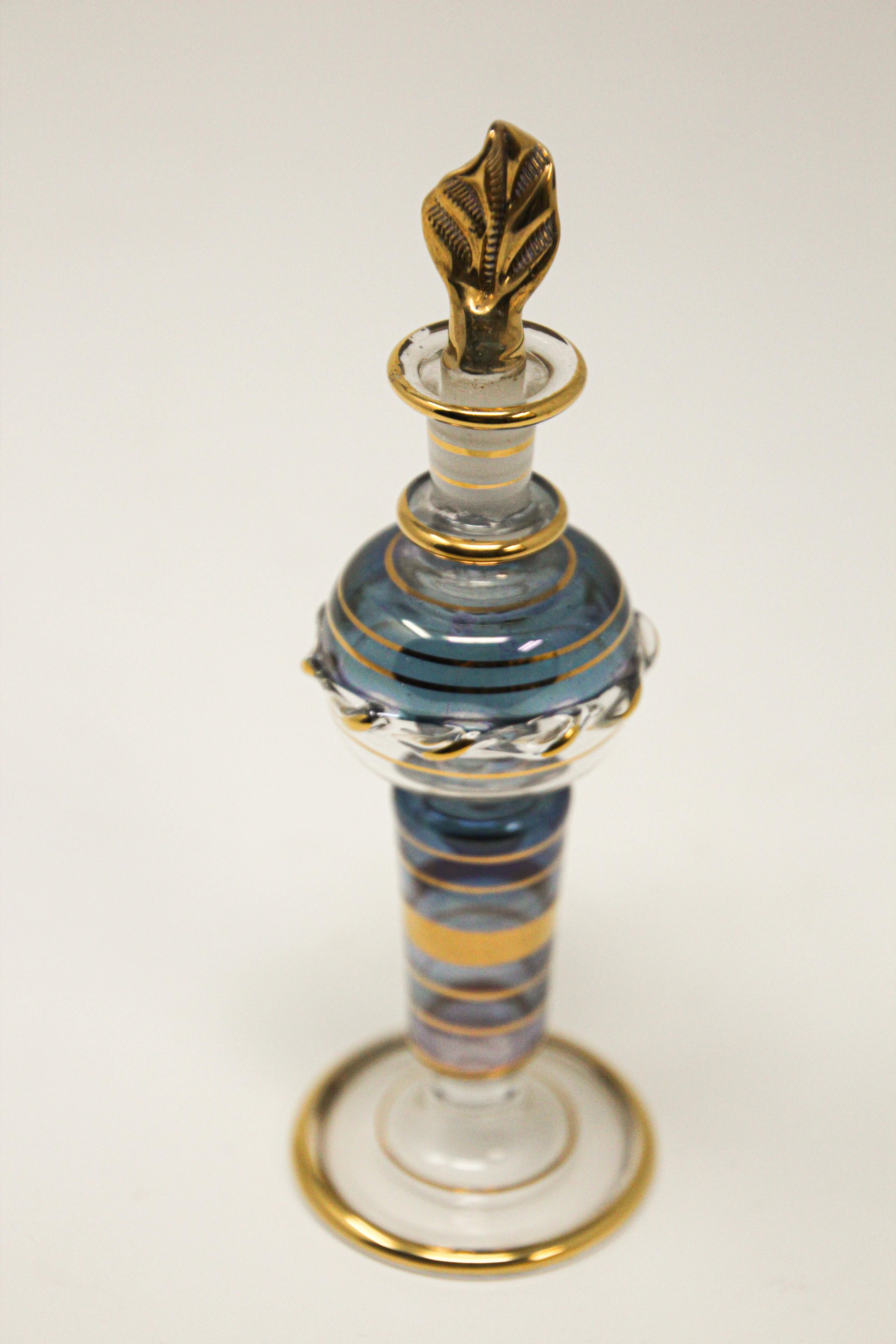 Handcrafted Moroccan Moorish gilt glass perfume bottle.
Hand blown glass perfume bottle gilded with 24-karat gold hand painted designs with beautiful translucent blue colors in Moser style.
Uniquely shaped leaf stopper has a glass applicator rod to