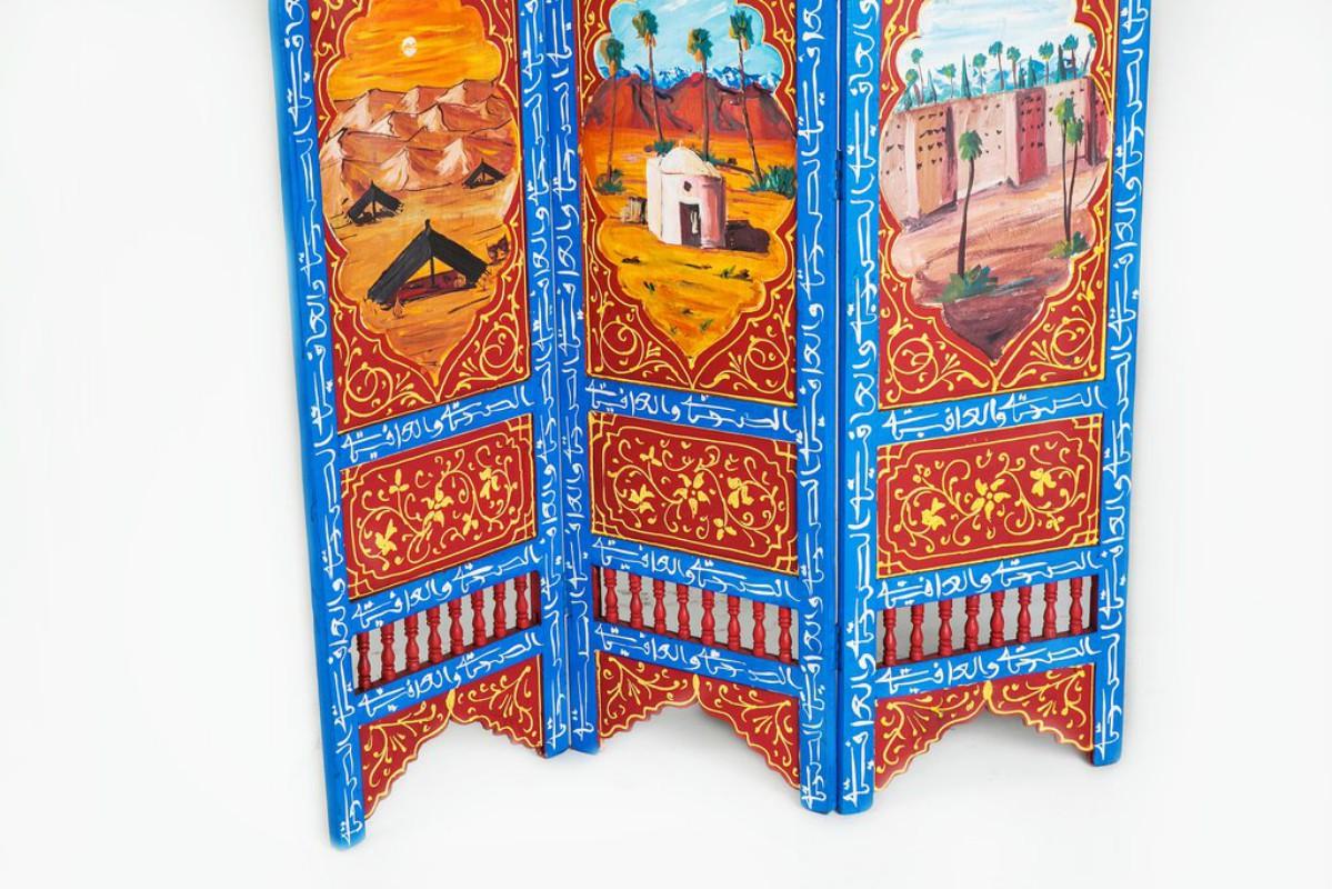 Hand-painted on wood and featuring an orange and blue color pattern, this divider features a triptych of tranquil images: the desert at sundown, a lone cabin bracketed by trees and the calming order of a city wall. With added swirling imagery and a