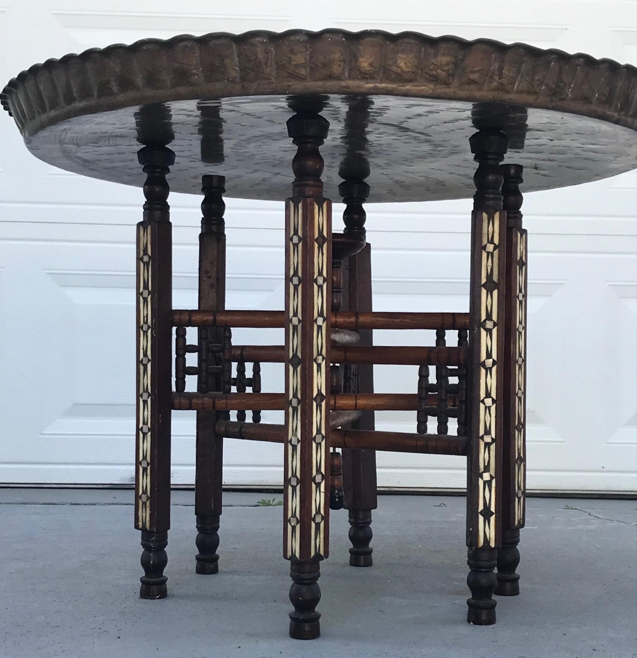 Moorish inlaid mother of pearl six legged brass tray top folding side table.

The inlay work makes this folding tray an exceptional handmade side table. An ebonized hand carved turned wood base of 6 legs is ornately inlaid with Arabic inspired