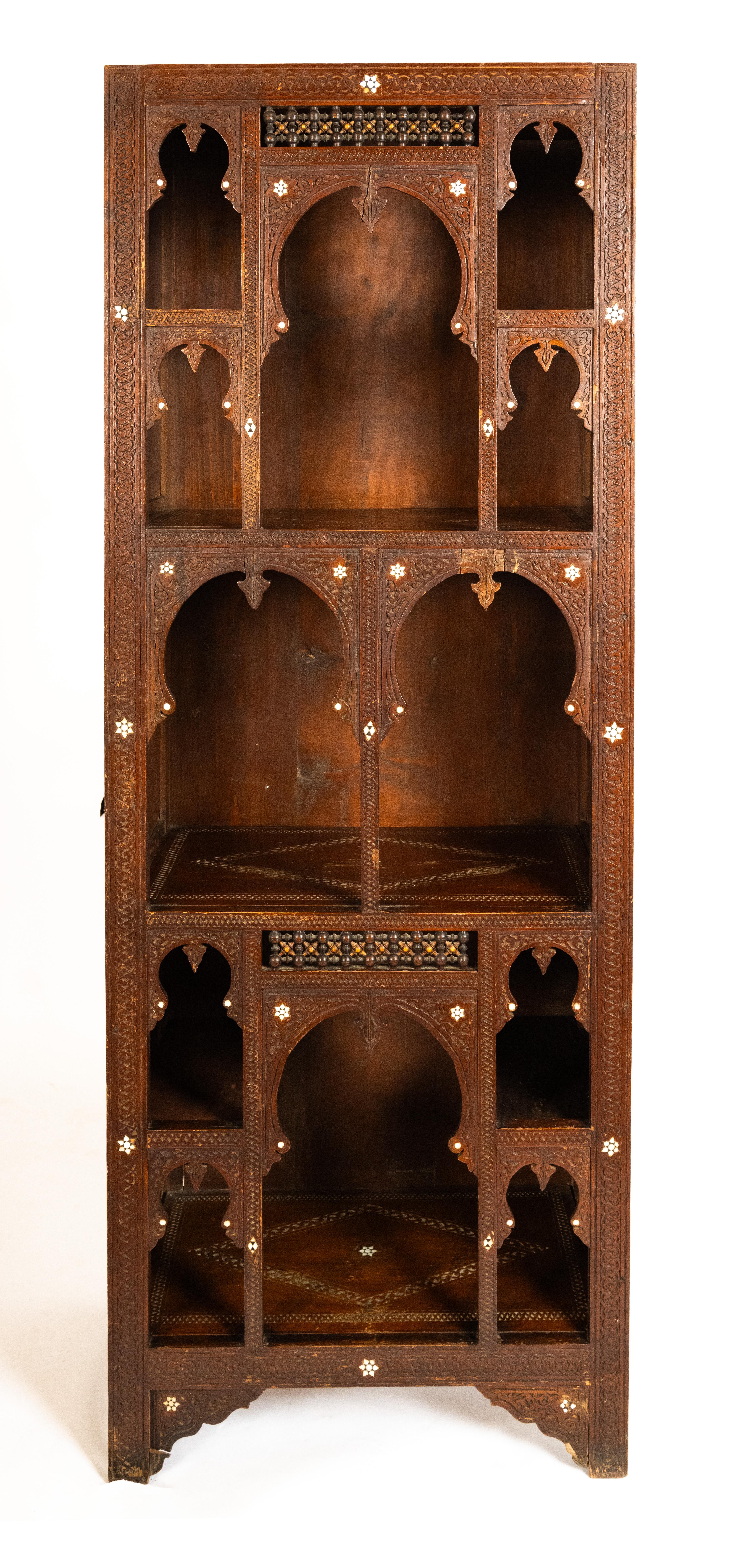 A free-standing vitrine of architectural form. With shelves of varying heights framed by Moorish arches having inlaid contrasting details. The rectangular frame with enclosed top, sides, and bottom are supported by bracket feet.