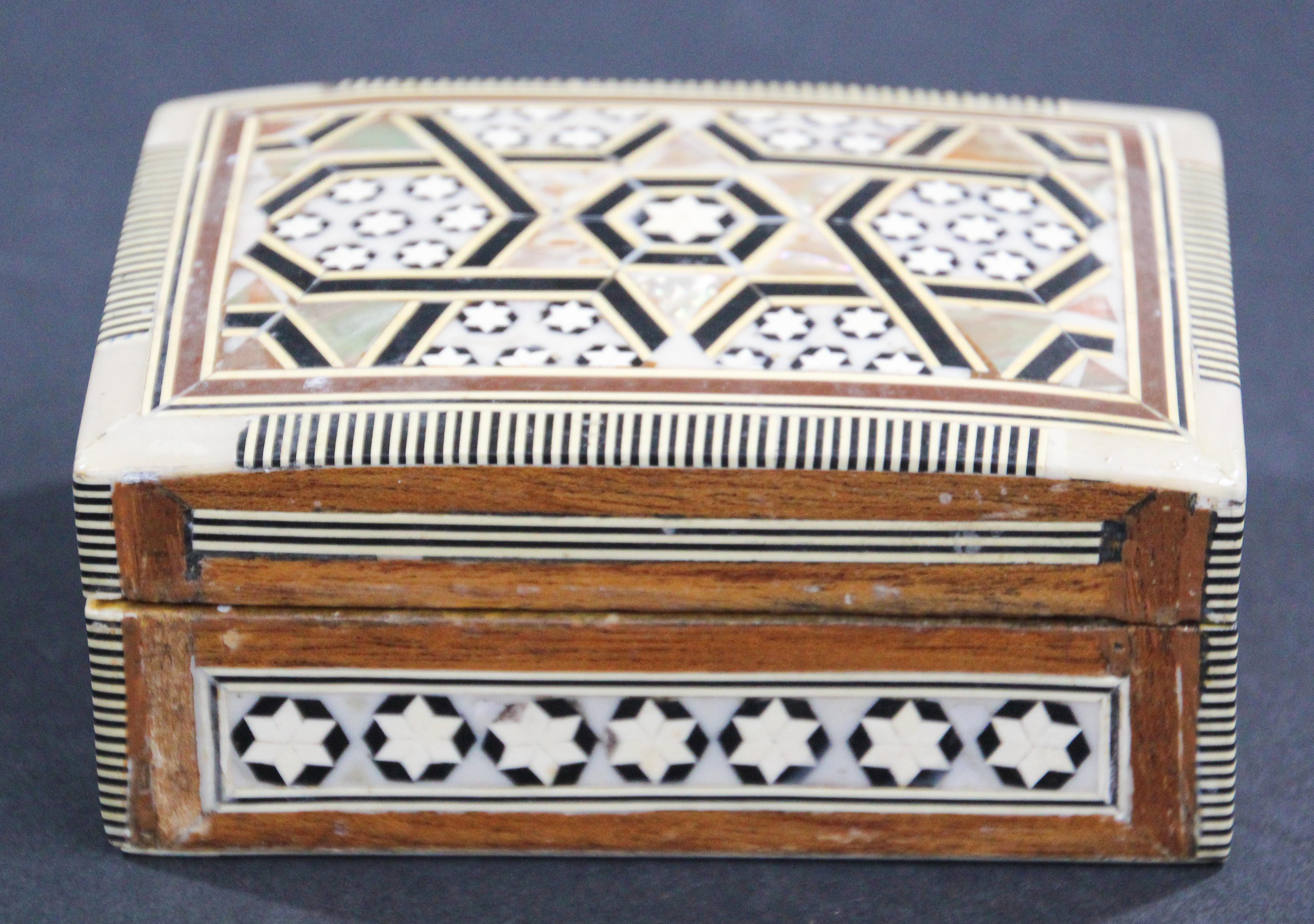 Boîte en bois de noyer incrustée de mosaïques du Moyen-Orient, fabriquée à la main.
Petite boîte décorée de façon complexe de motifs mauresques en forme d'étoile de David qui ont été minutieusement incrustés de marqueterie de mosaïque, de nacre et