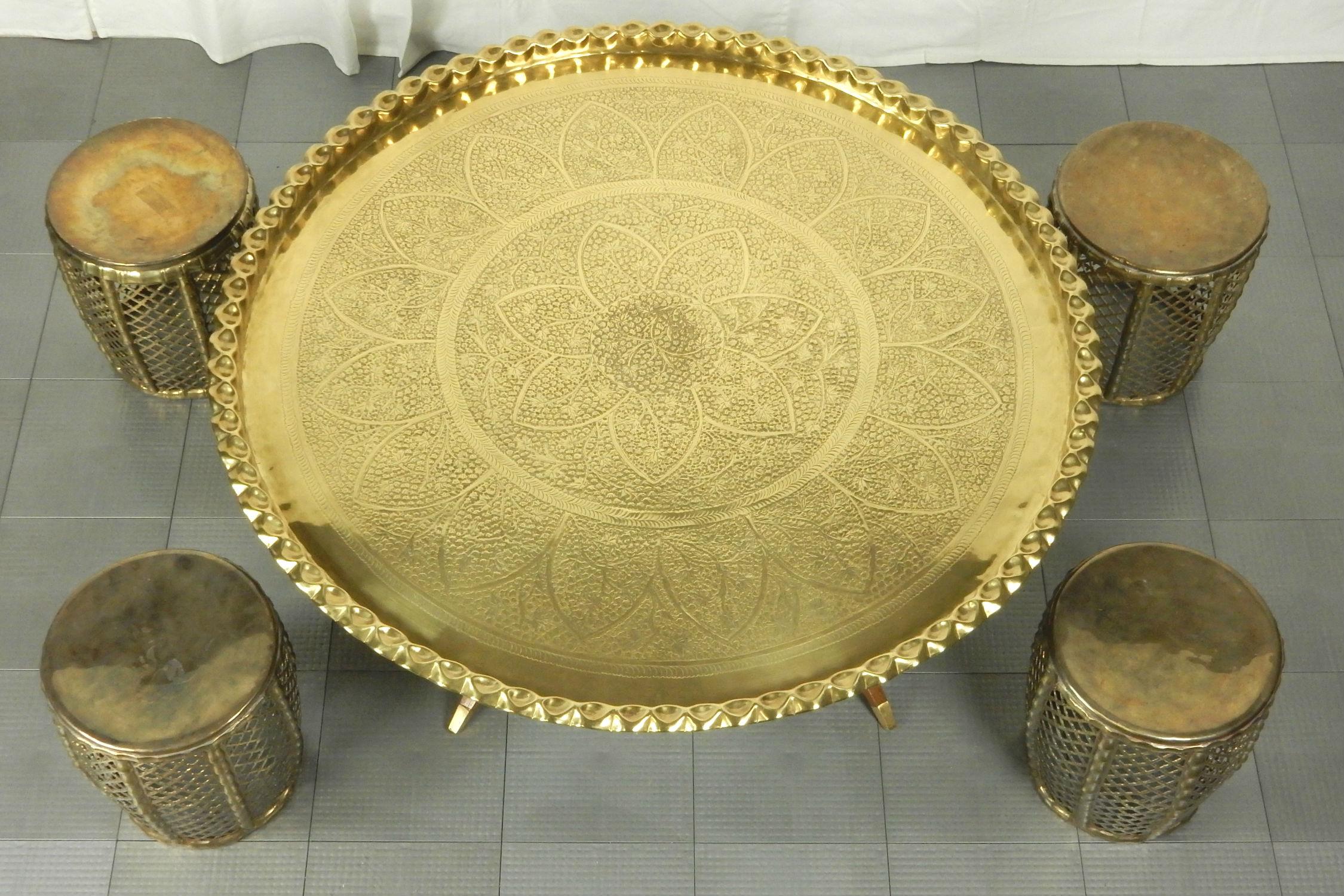 Mid-20th century large tooled brass tray on spider base coffee table with 4 stools. Clean, better than average condition.
Perfect arrangement for an eclectic home decor. 
Measures: 44 inch round tray X 16-1/2 inch tall, each stool 12 inch X 12 inch.