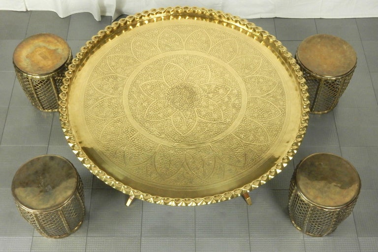 Mid-20th century Moorish/Moroccan large tooled brass tray on spider base coffee table with 4 stools.
Perfect arrangement for an eclectic home decor. 
Measures: 44 inch round tray X 16-1/2 inch tall, each stool 12 inch X 12 inch.