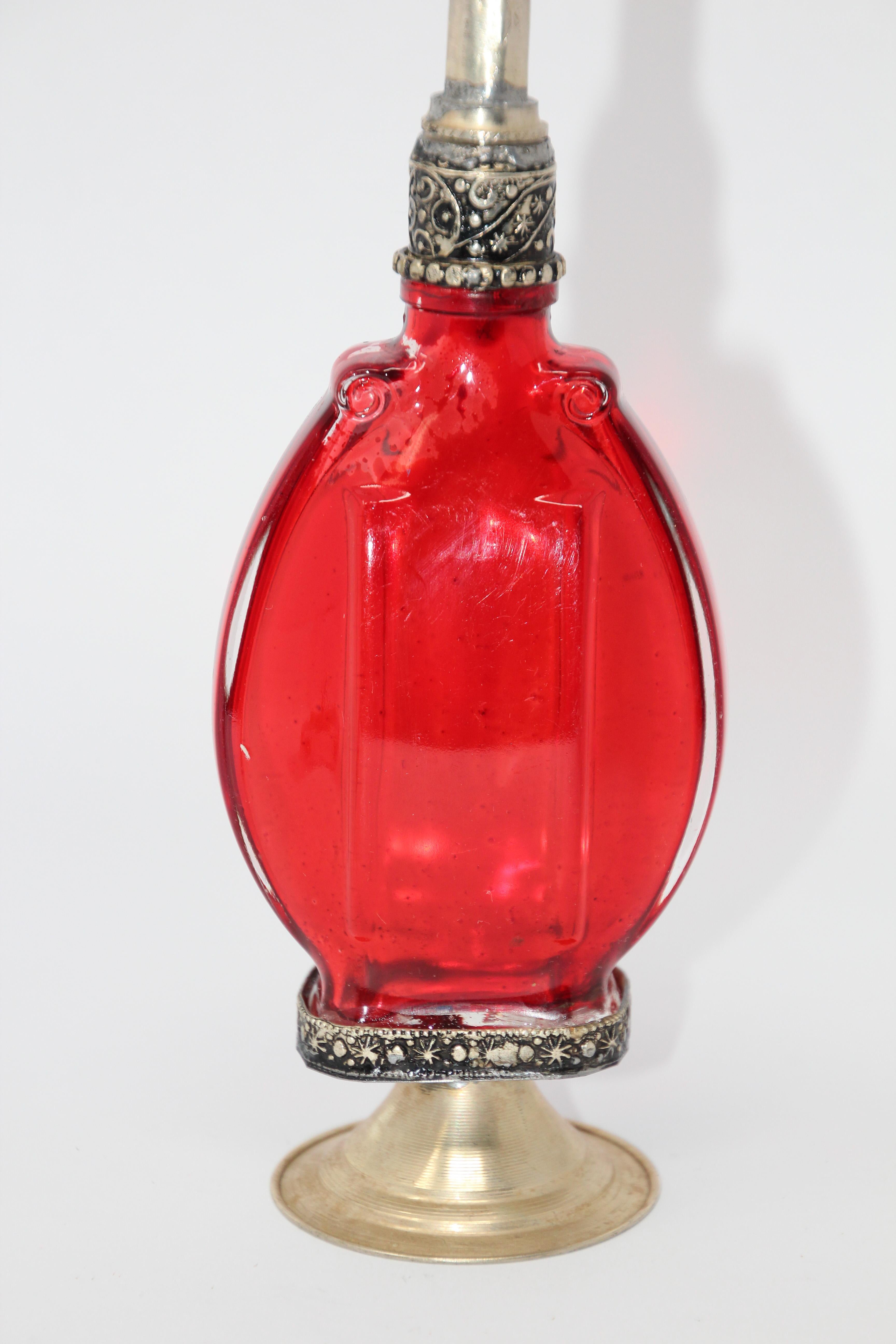 Handcrafted Moroccan Moorish red glass perfume bottle or rose water sprinkler with raised embossed silvered metal floral design over red glass.
The pressed glass bottle in Art Deco, Art Nouveau style is oval shape with curved sides and hand