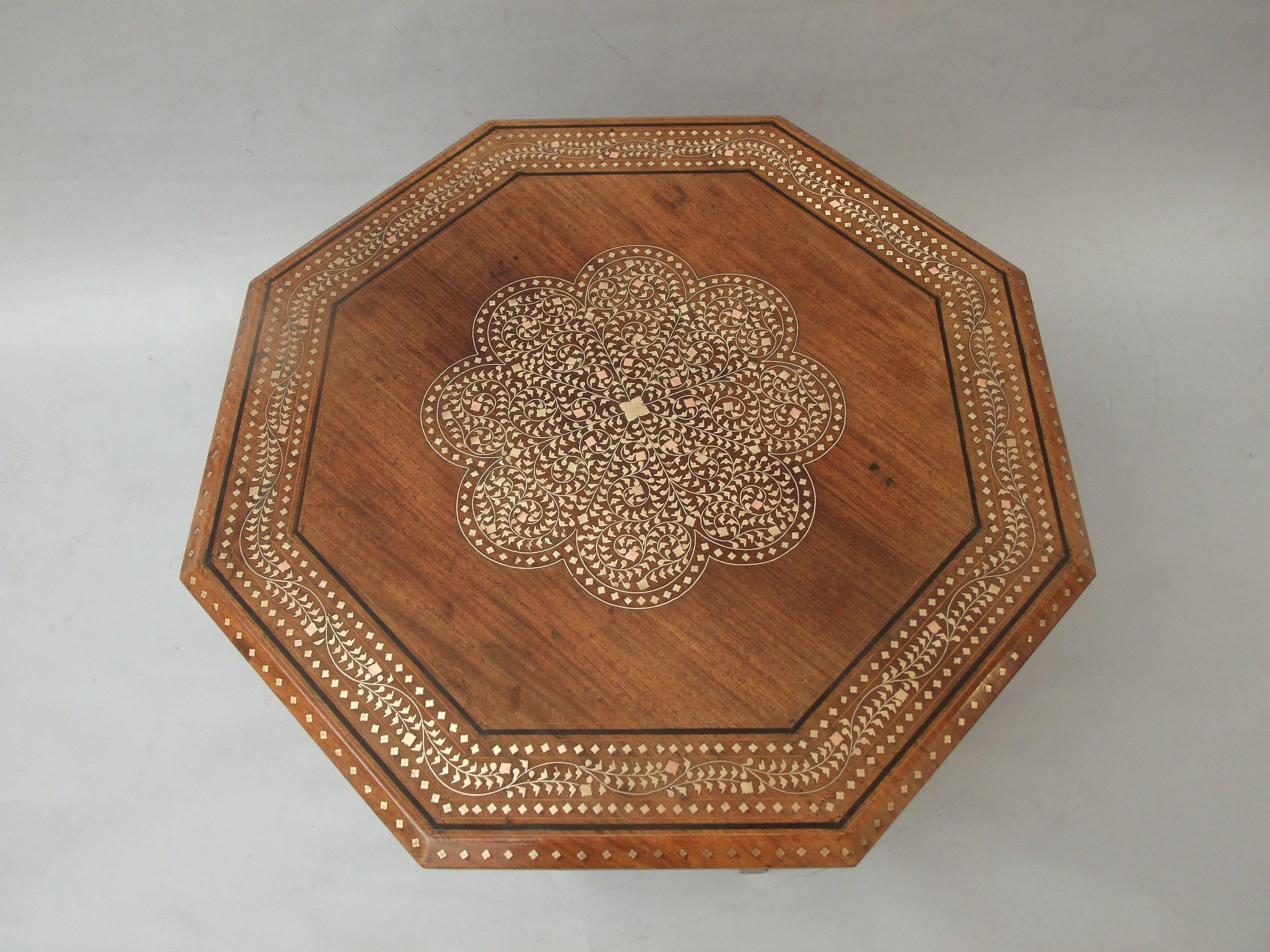 A Moorish, teak, folding occasional table, Moorish arches between the supports, profusely inlaid in copper and brass foliate design, retailed by Liberty's, circa 1900. Measures: 41cm (16in) high, 66in (26in) wide.