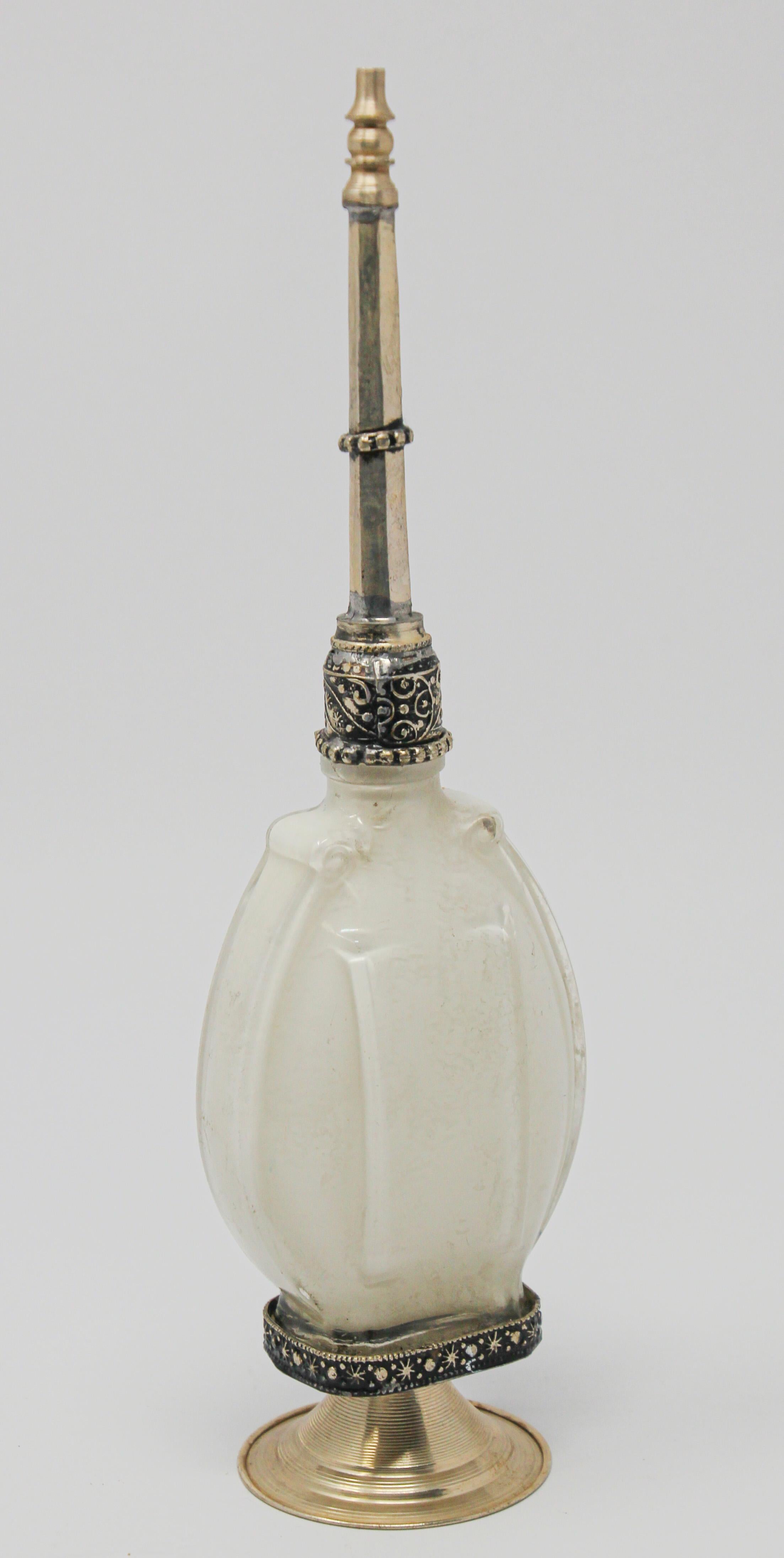 Handcrafted Moroccan Moorish white glass perfume bottle or rose water sprinkler with raised embossed silvered metal floral design over amber glass.
The pressed glass bottle in Art Deco, Art Nouveau style is oval shape with curved sides and hand