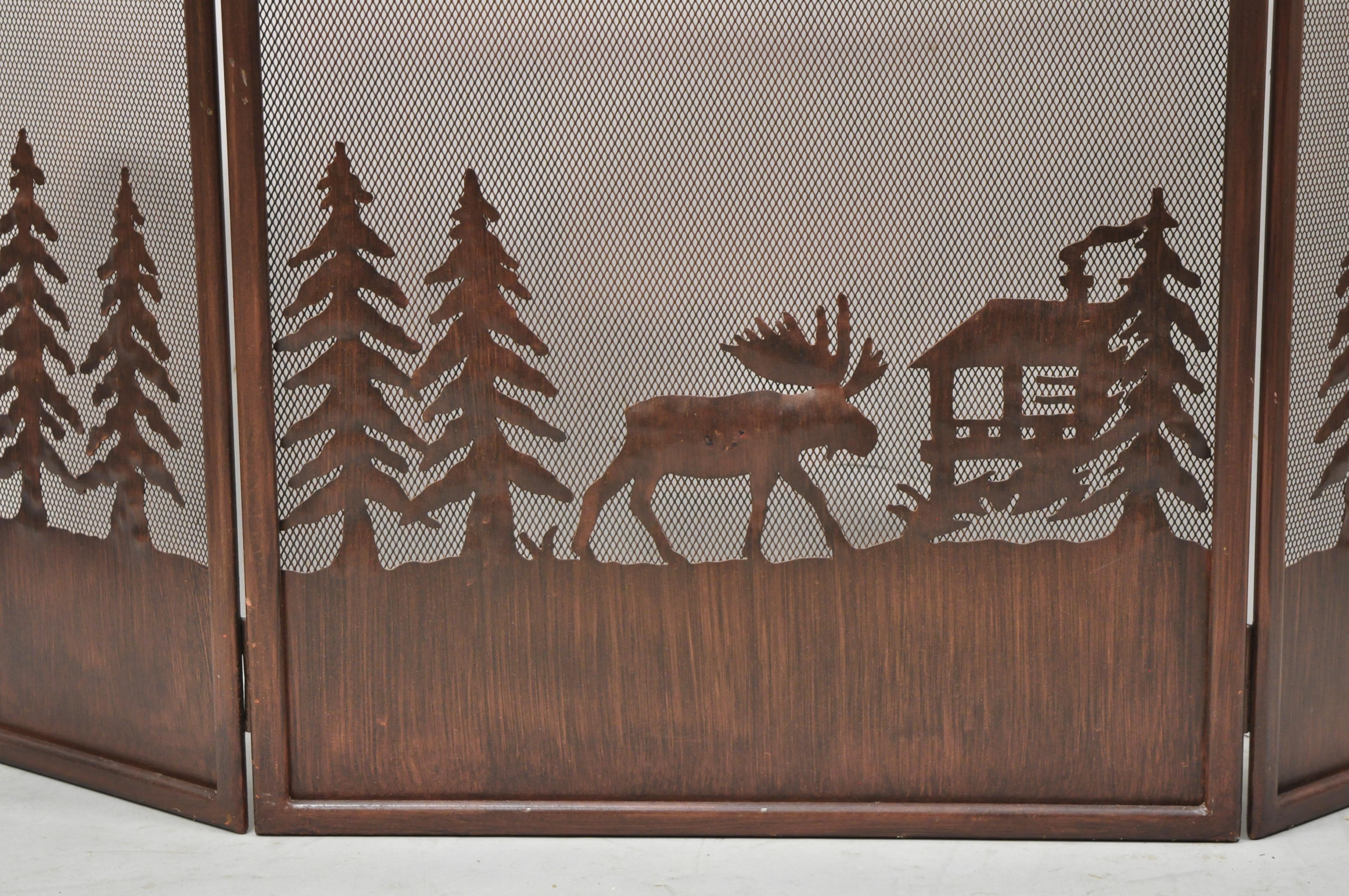 Moose wilderness log cabin rustic iron folding fireplace mantle screen. Item features 3 section folding screen with wilderness scenes of tall trees, a moose, and log cabin. Age: Late 20th century. Measurements: 30