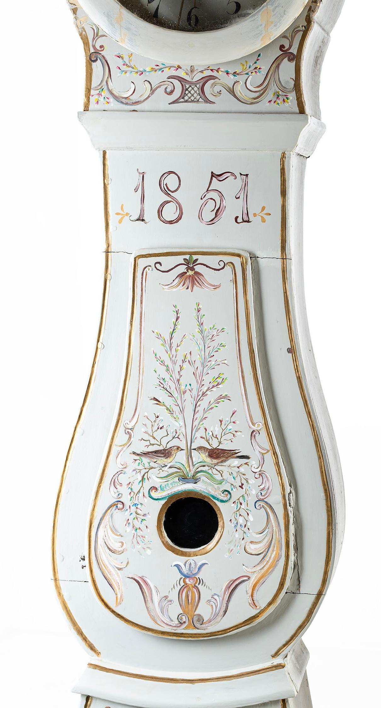 Pendule Mora suédoise de 1851 avec des détails floraux peints à la main sur un fond peint en blanc (peinture d'origine). Couronne sculptée. Les détails du cadran comprennent le nom de l'horloger : Anders Matsson et le village Mora. Mécanisme