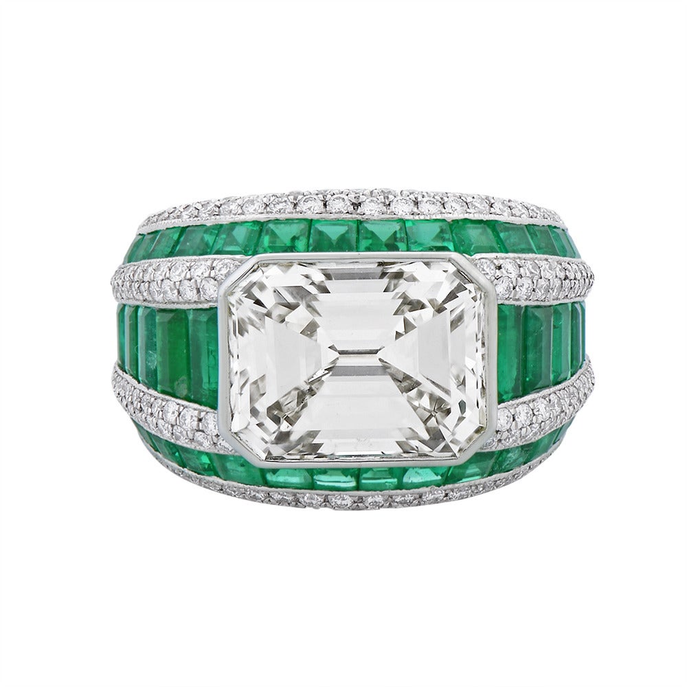 A stylish contemporary diamond and emerald ring set with a 5.82 ct emerald-cut diamond (cape color, VS clarity) as the centre stone in a platinum shank channel set with baguette-cut and calibré-cut emeralds spaced by double rows of pavé-set diamonds.